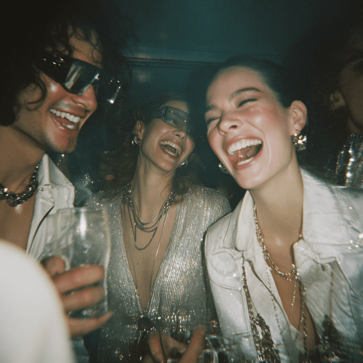 Friends laughing and celebrating with drinks in a candid, dark party setting.