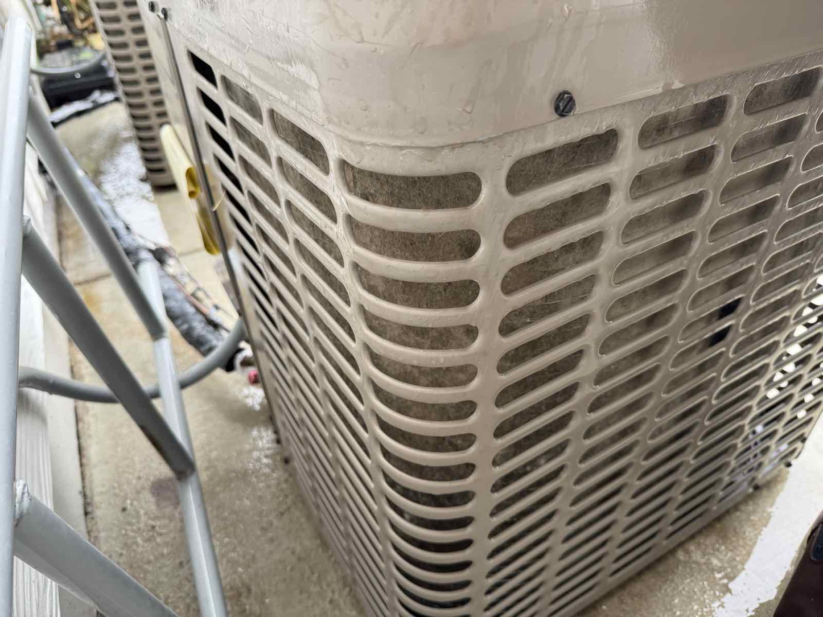 A close view of an outdoor air conditioning condenser with cottonwood debris matted between the aluminum fins.
