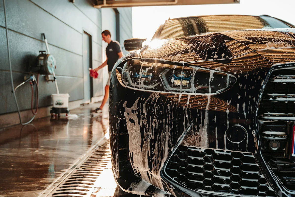 Luxury car undergoing professional detailing wash with foam cleaning at an auto care facility.