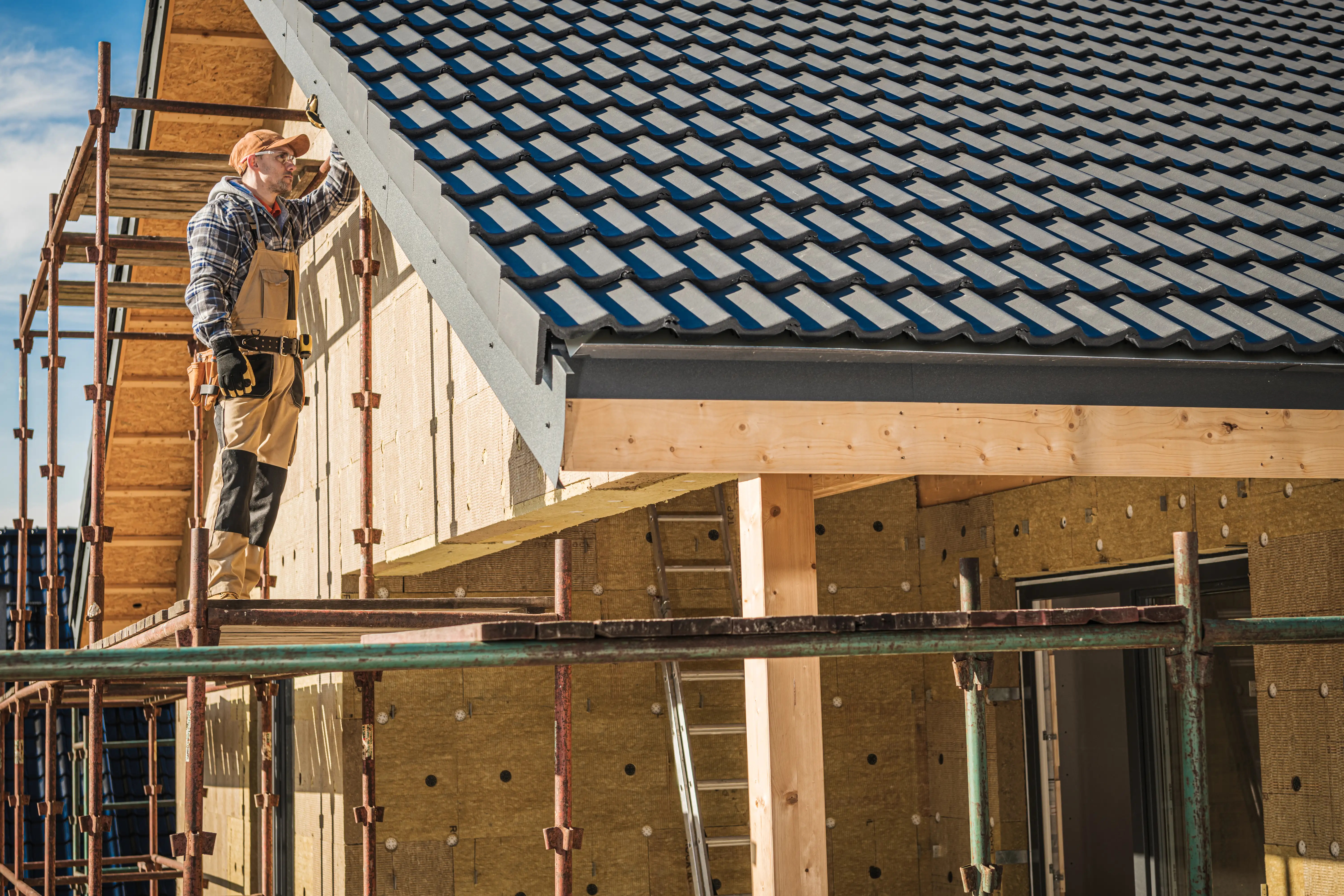 Roofer working on installing dark tiles onto the roof of a residential house under construction.