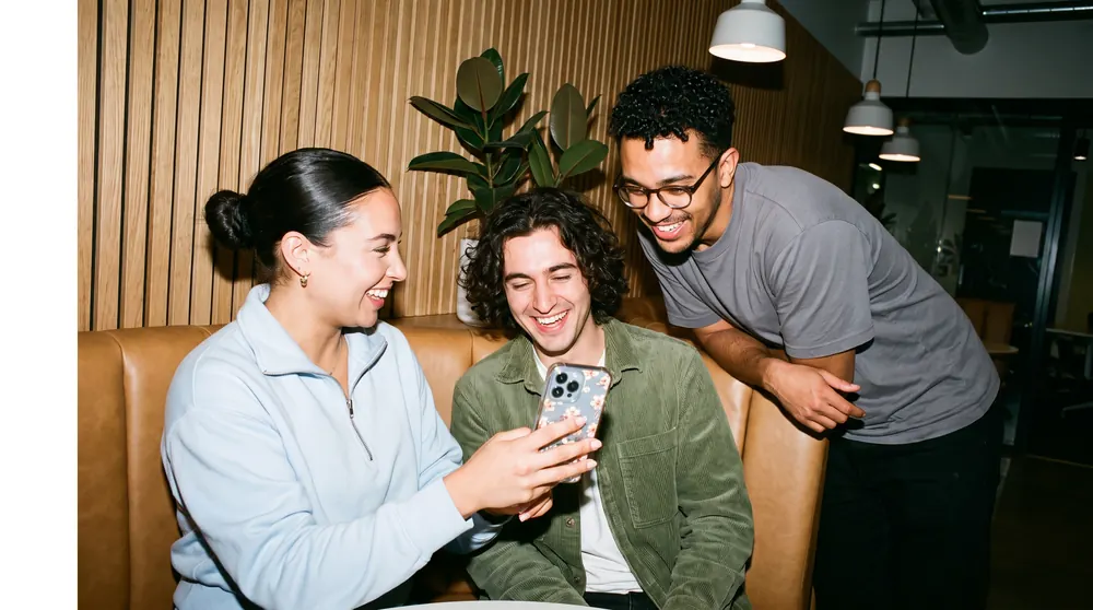 Three colleagues laughing over a phone in a booth
