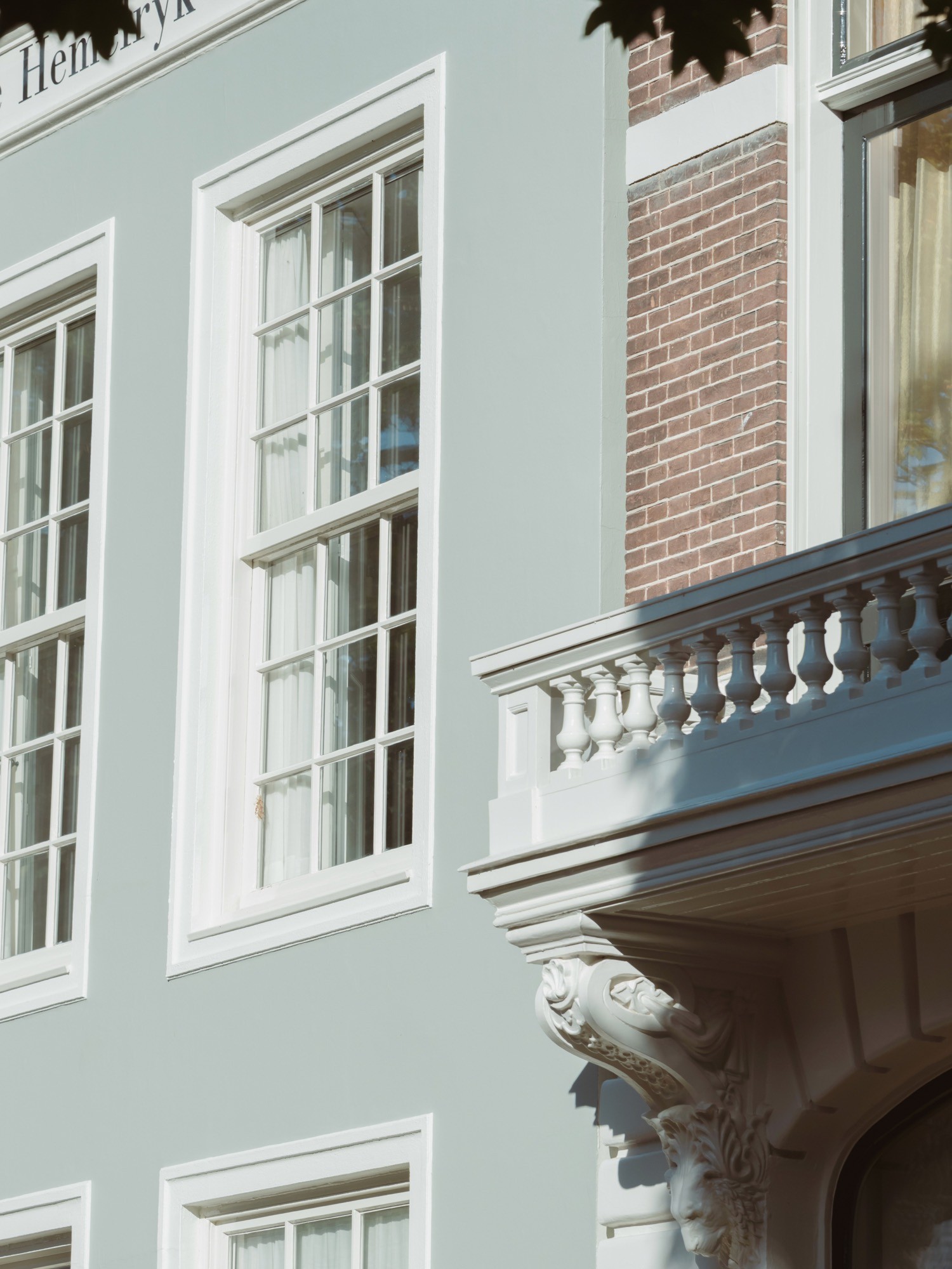 Lichtgroen gepleisterde monumentale gevel met witte kozijnen en een balkon met balustrade