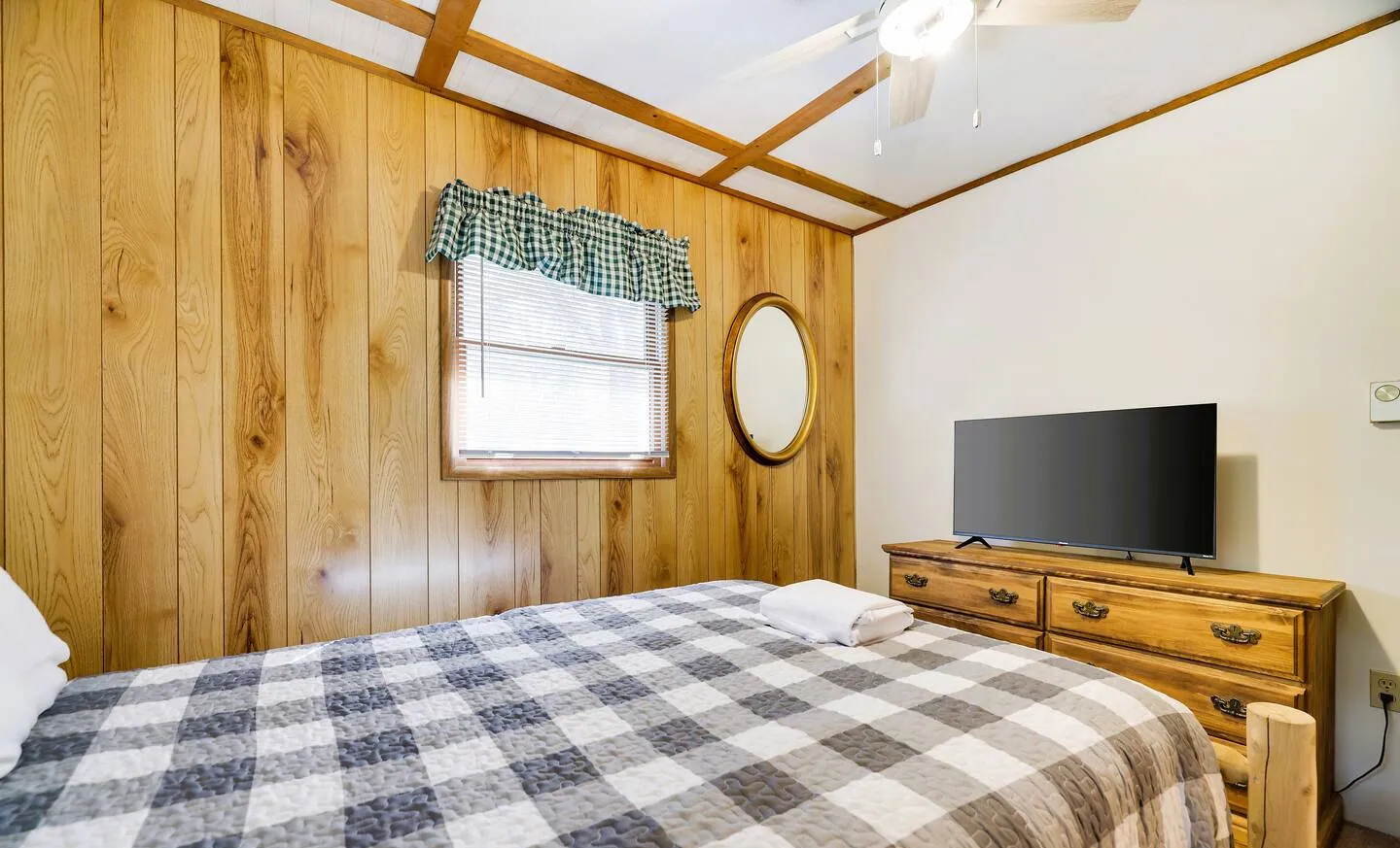 Queen bedroom with pine paneling, checked quilt and TV on dresser at RedHawk Chalet