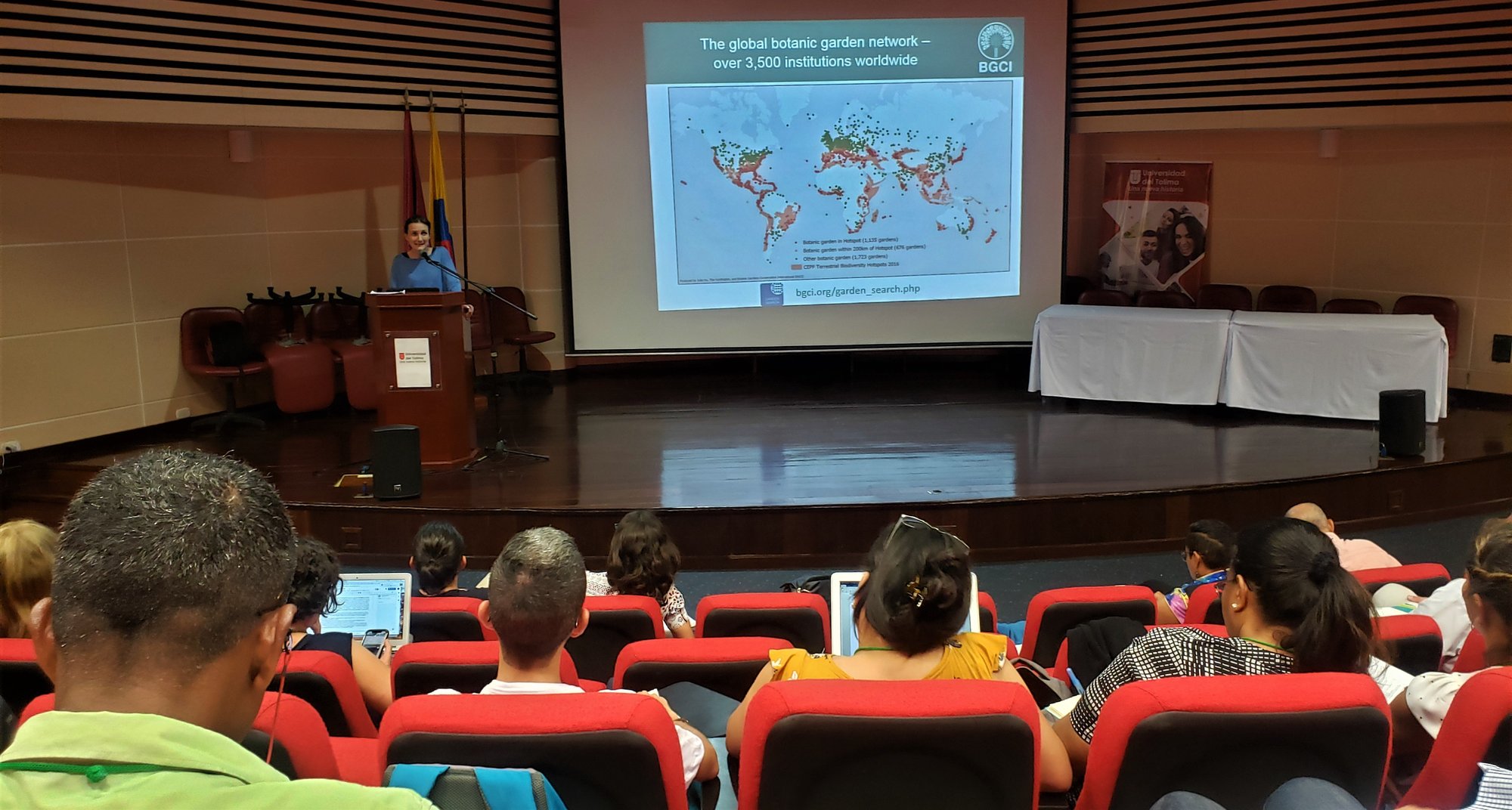 Plateia em auditório assiste a apresentação com mapa-múndi projetado no telão