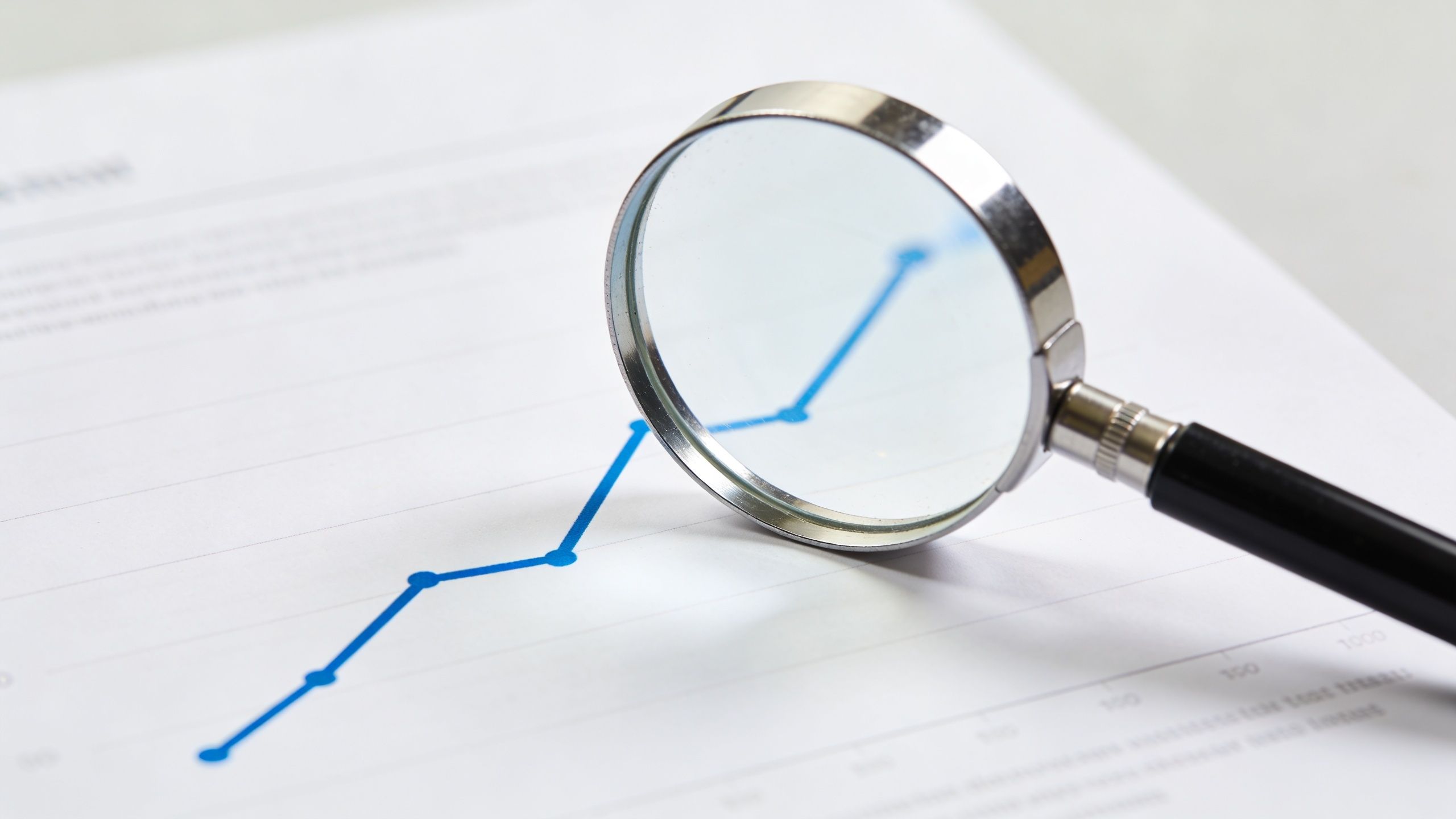A magnifying glass focusing on a blue line graph representing positive growth on a document.