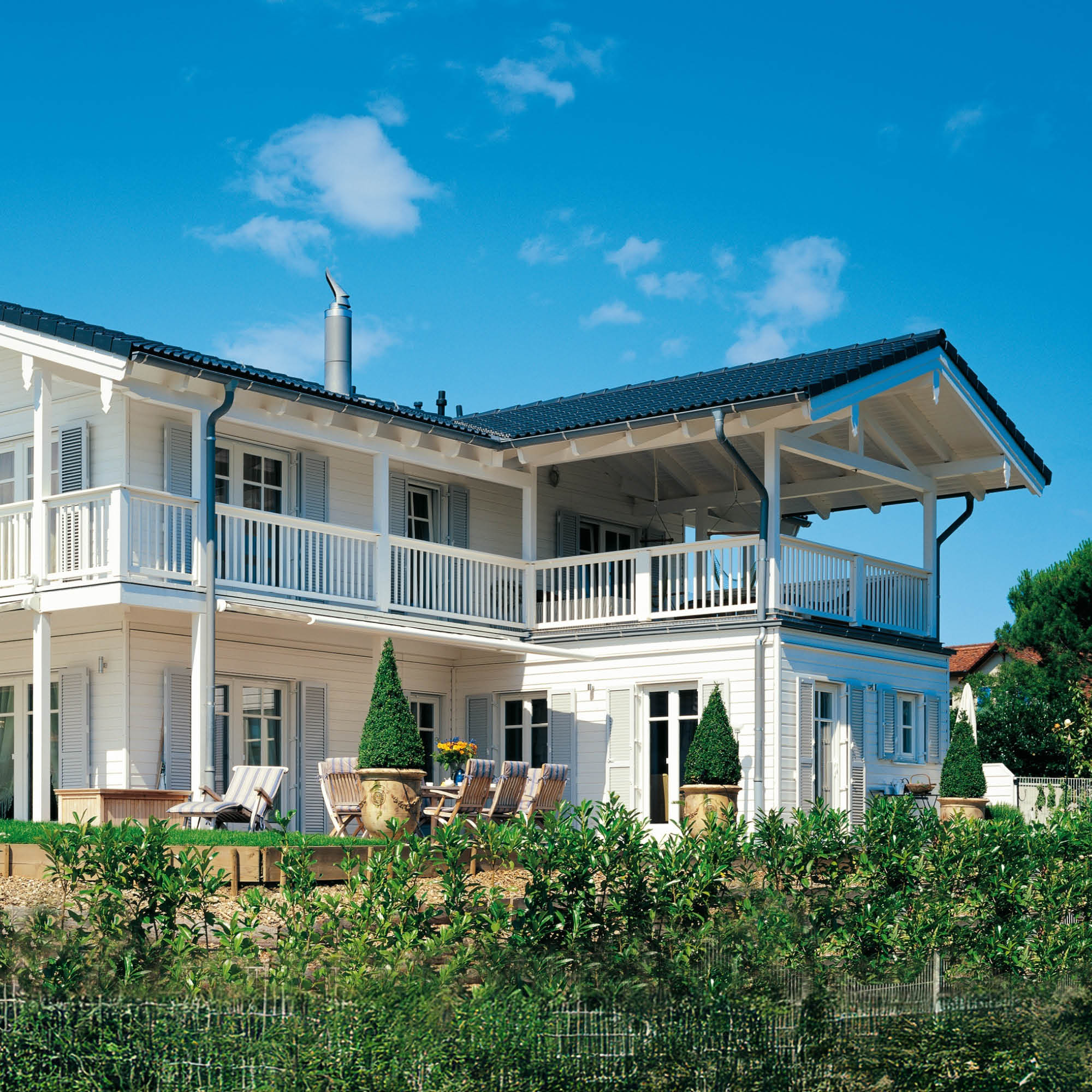 Dreistöckiges weißes Einfamilienhaus mit Balkonen, Schornstein und gepflegtem Garten.