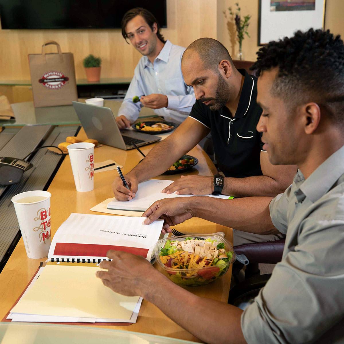 An overhead shot of a large oval plate featuring sliced, roasted duck, half glazed with a sauce, served over two thin pancakes and alongside steamed bok choy, surrounded by small bowls of condiments like scallions, sauce, salt, and carrot shreds.
