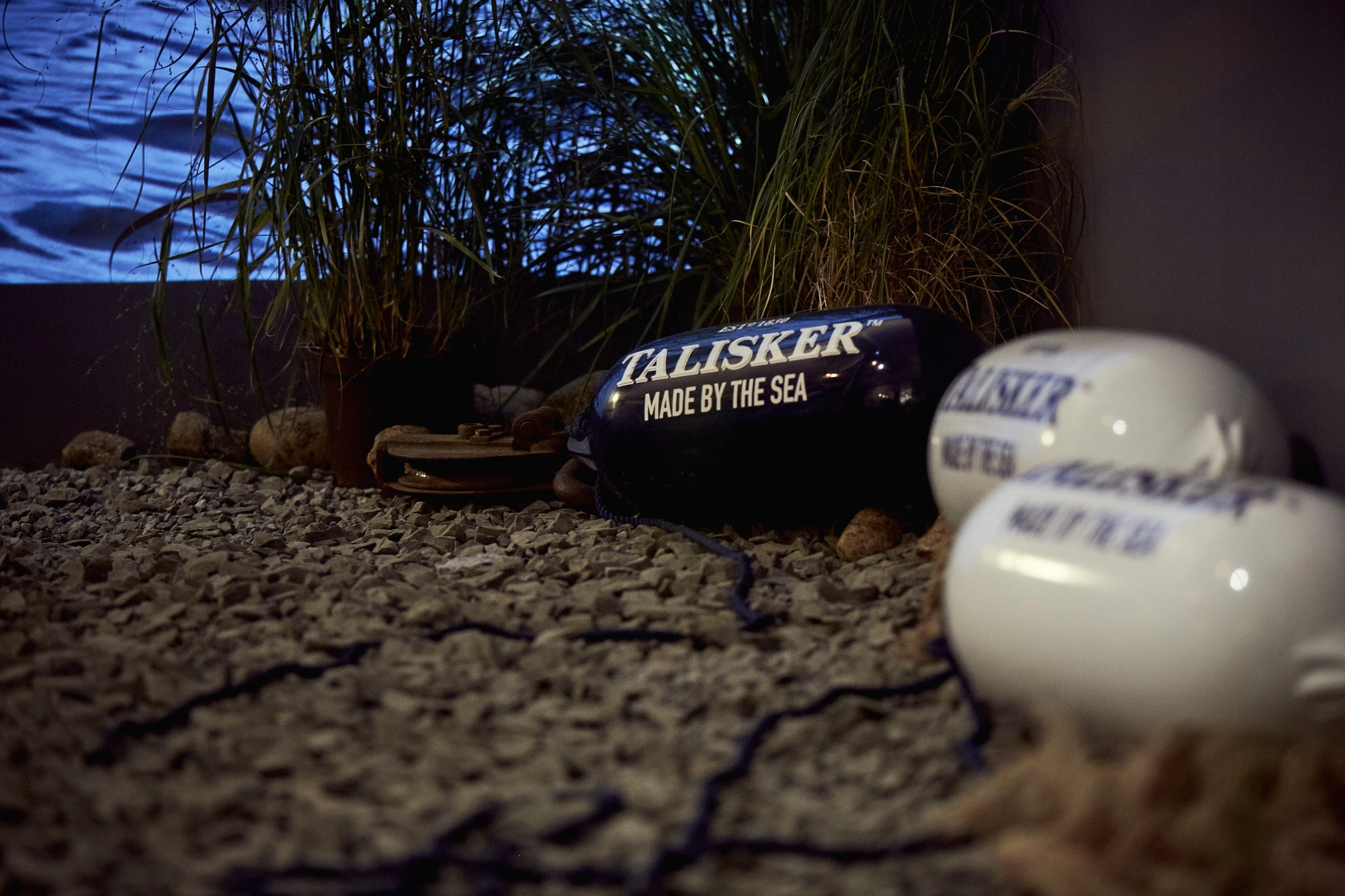 Talisker buoys with Made by the Sea lettering lying on pebbles between dune grass at DIAGEO BCB17.