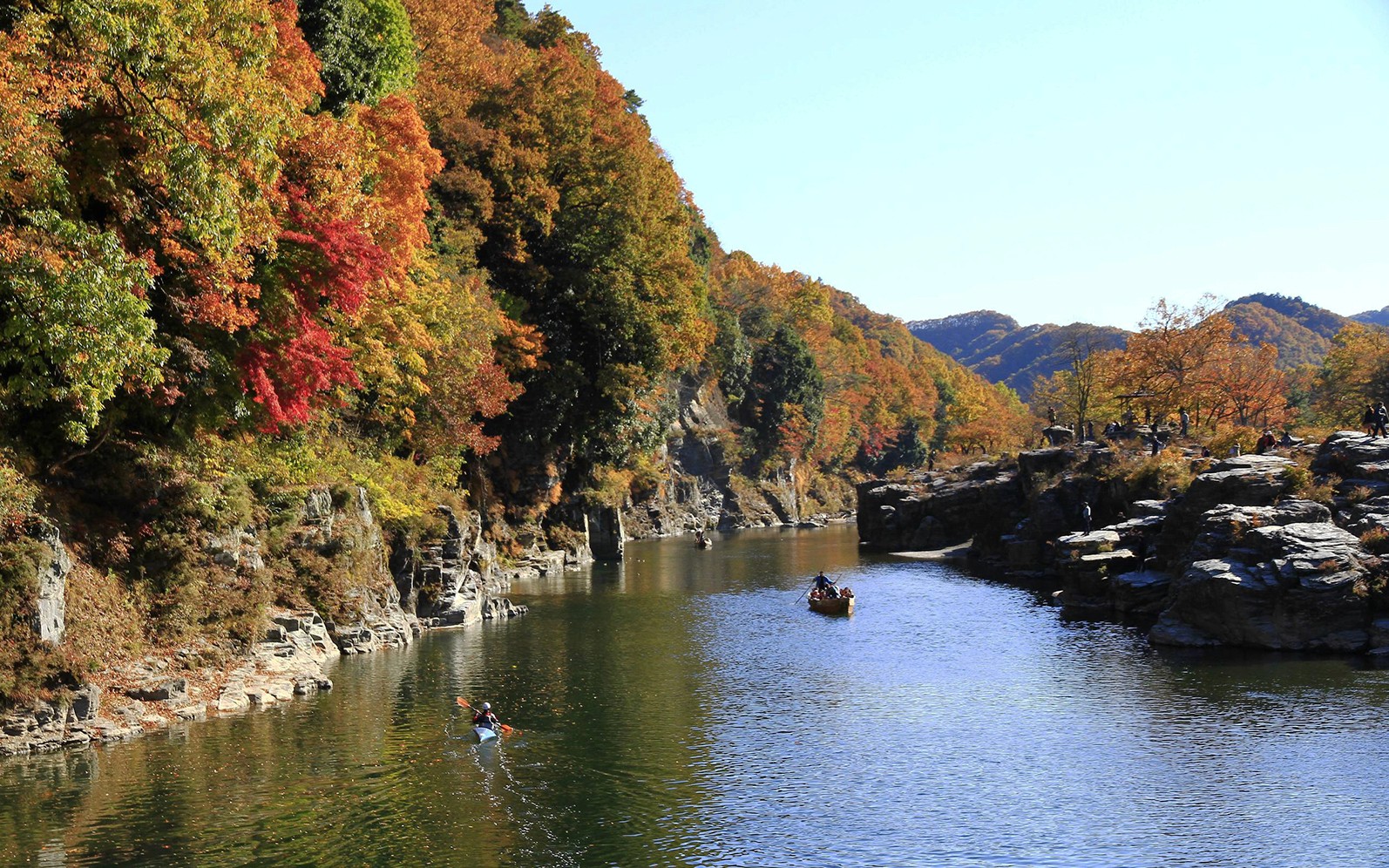 Kayakers on a river surrounded by autumn foliage in Chichibu, Japan.