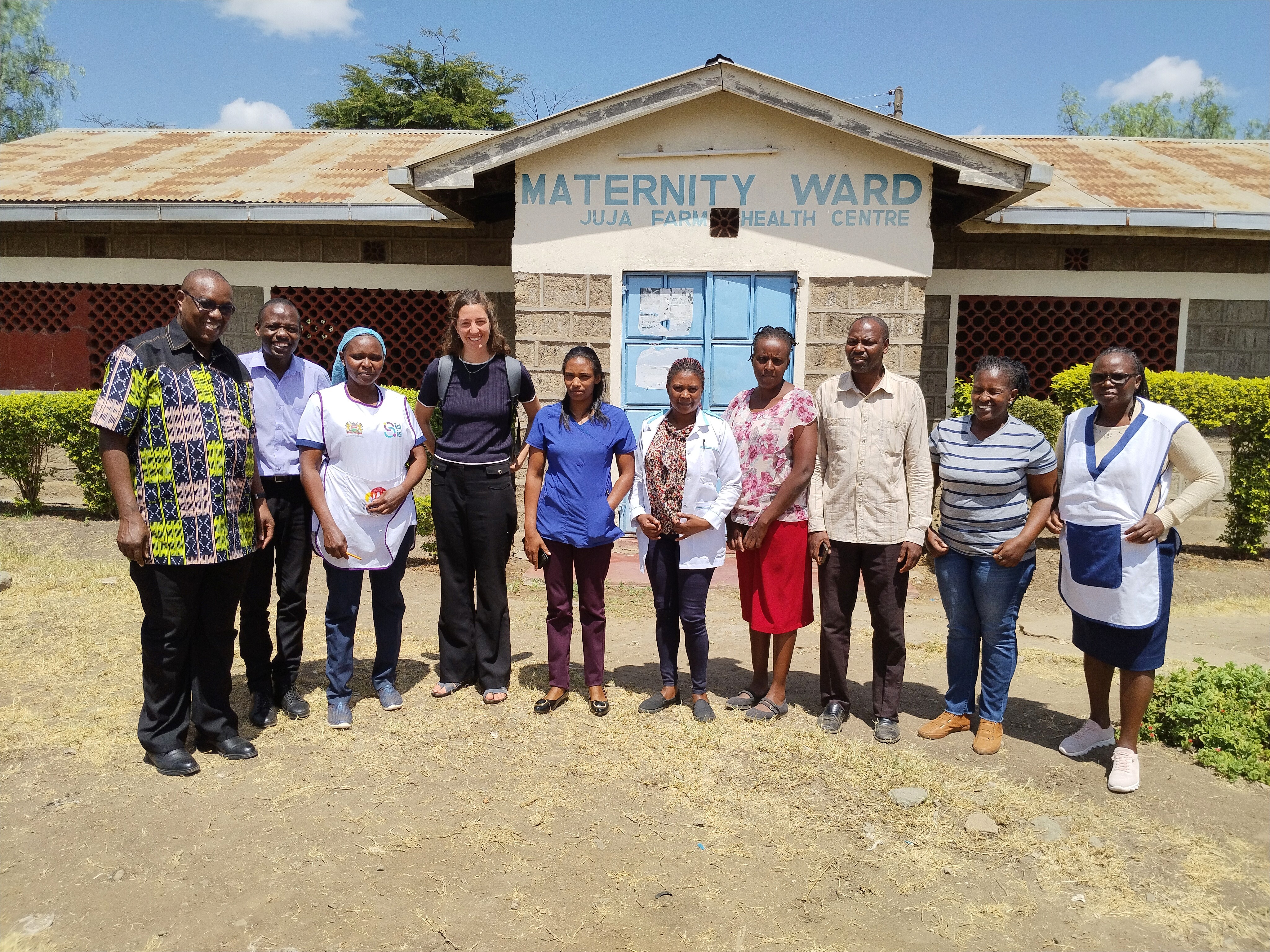 A smiling young man with crossed arms, wearing a plaid shirt and white t-shirt, poses against a dark background.