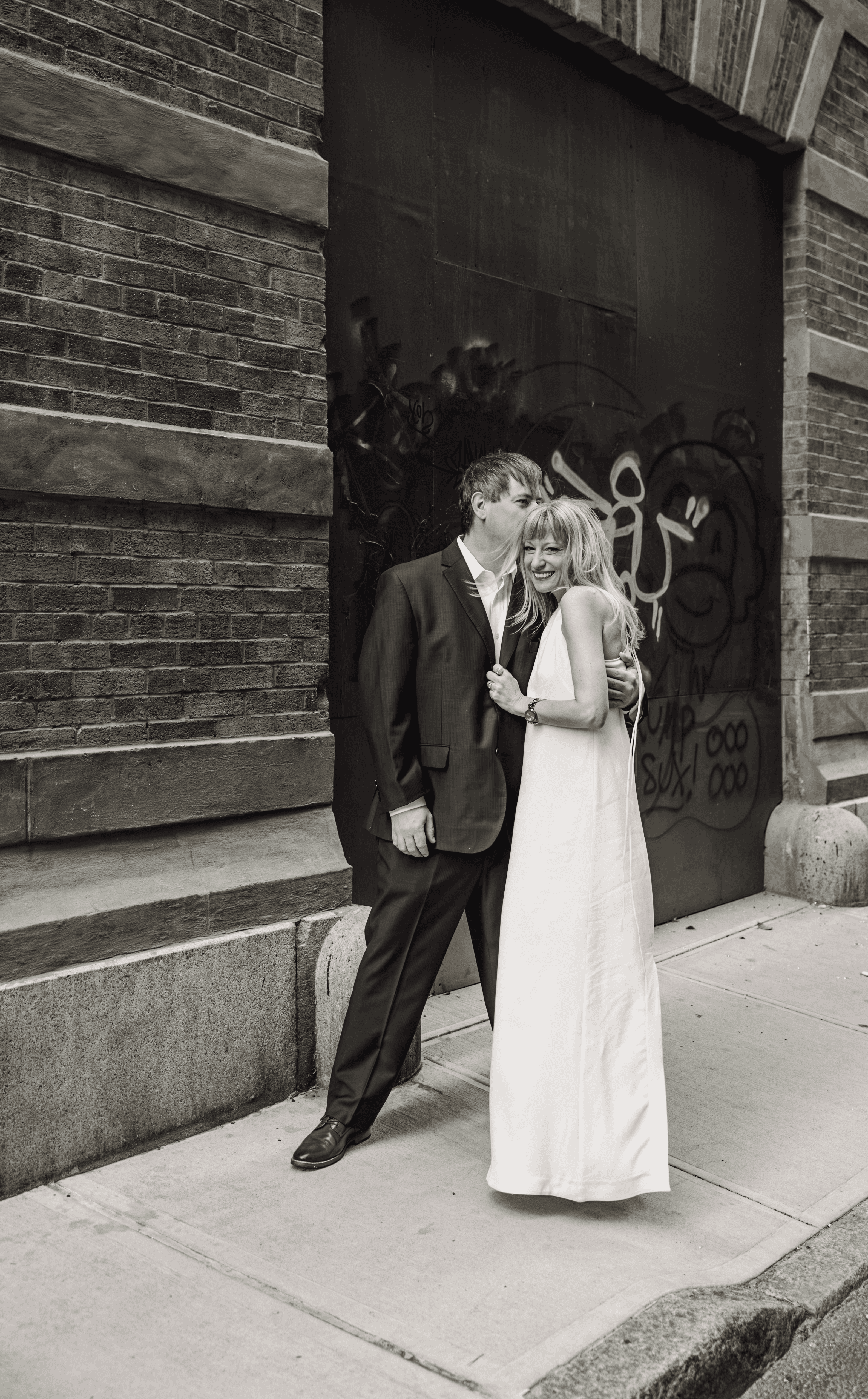 She's leaning in close, whispering in his ear beneath the iconic Staple Street Bridge in downtown Tribeca, NYC — intimate, romantic couples photography by Lizz Spano Photography, New York City couples photographer.