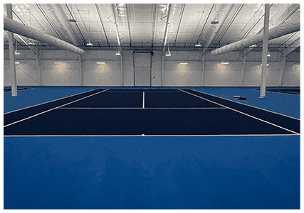 Indoor tennis court with blue acrylic playing surface and white court lines