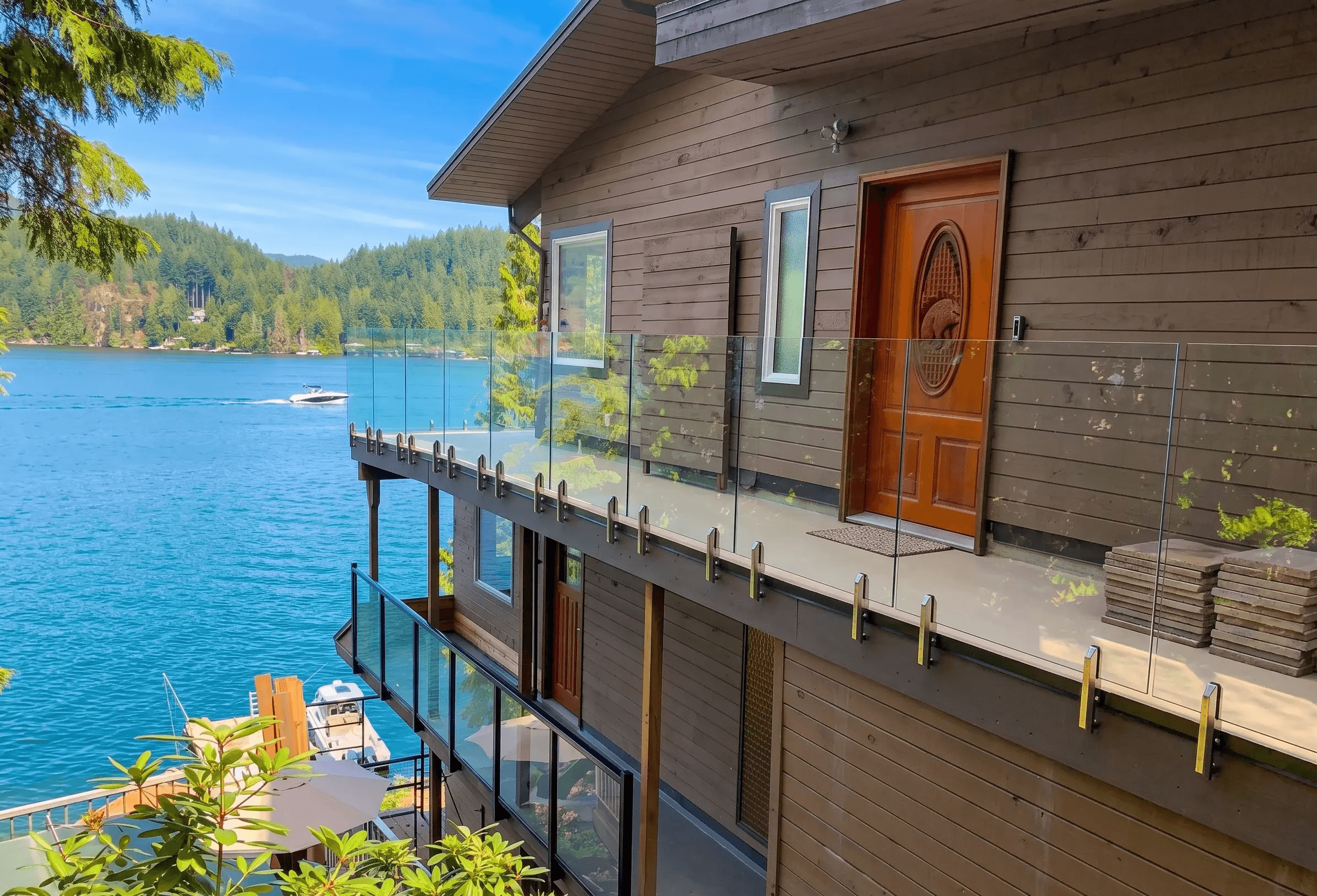 A side-angle view of a multi-level waterfront wooden house overlooking a vibrant blue lake on a sunny day.