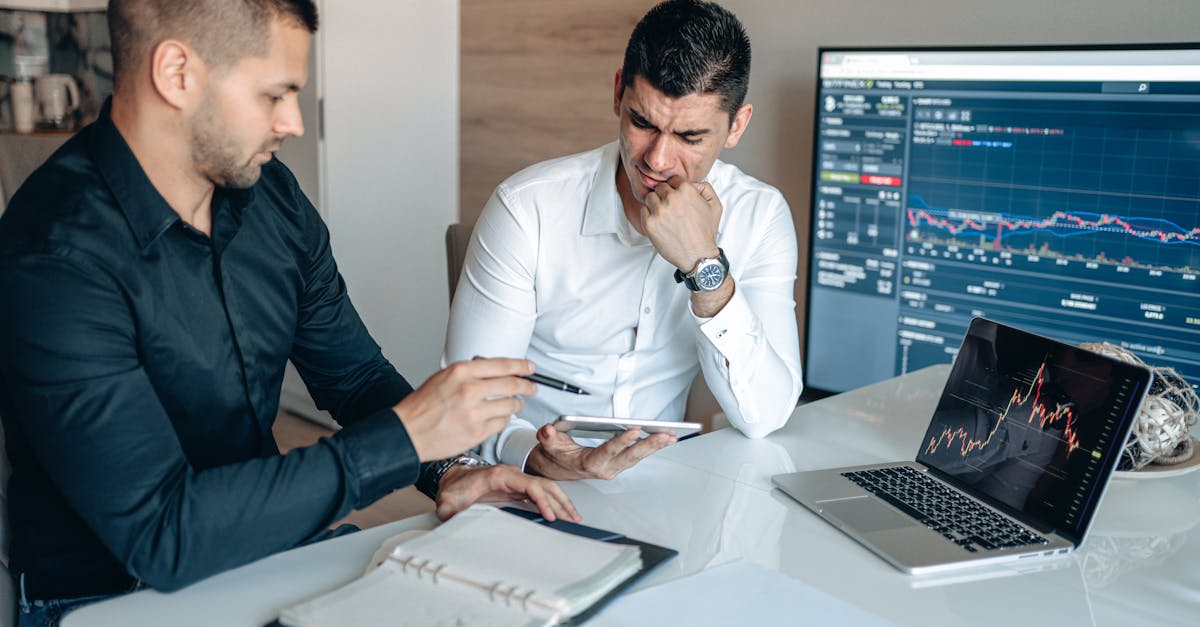 Two men discussing business analytics in an office with laptops and graphs.