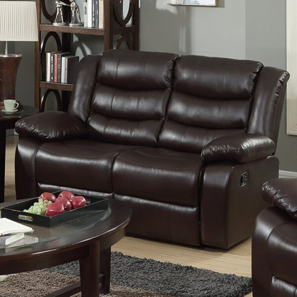 Dark brown faux leather reclining loveseat is placed in a living room with an oval wooden coffee table.