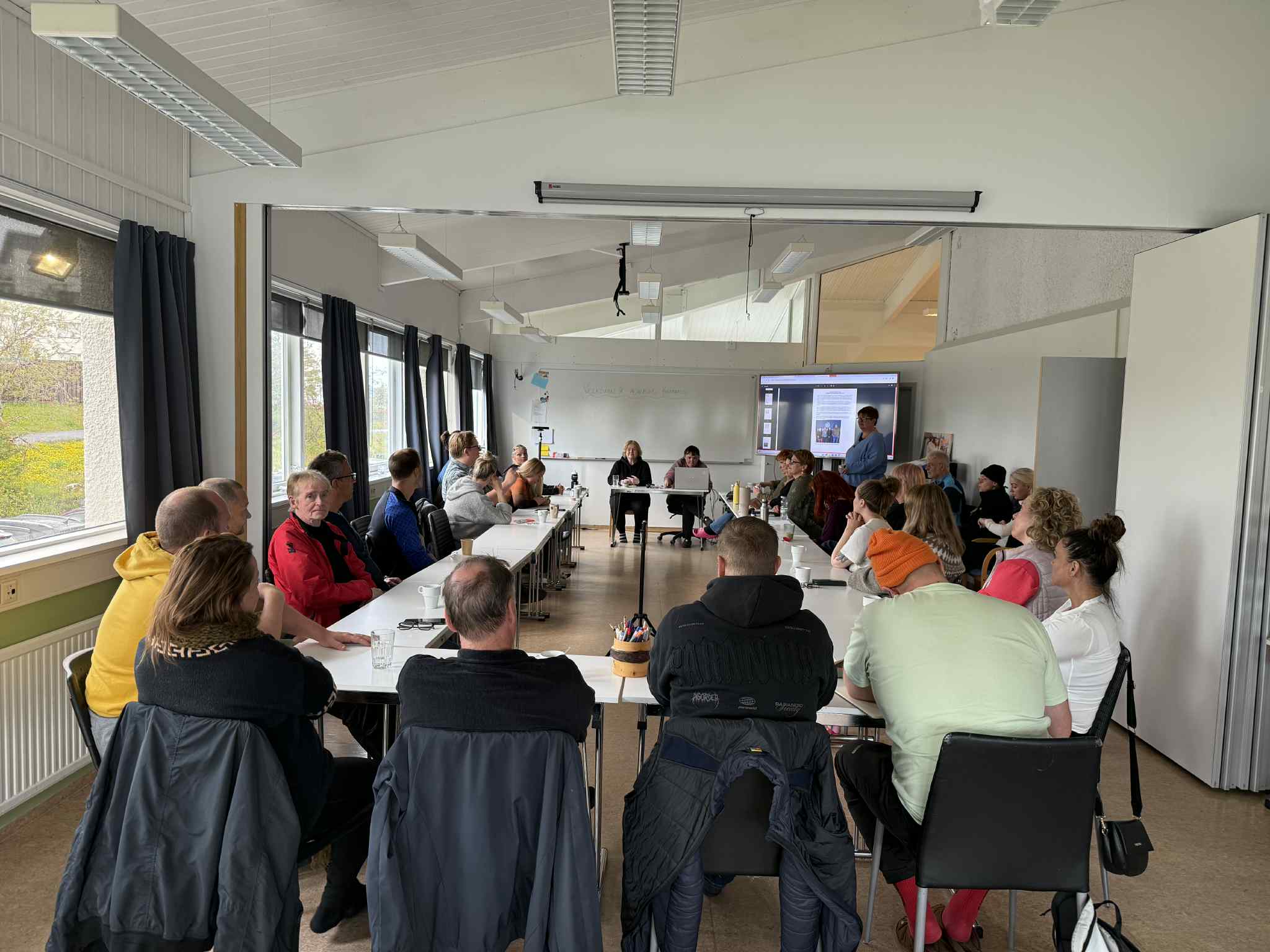 A woman with red hair and a black sleeveless top smiling confidently in a bright, modern indoor setting.