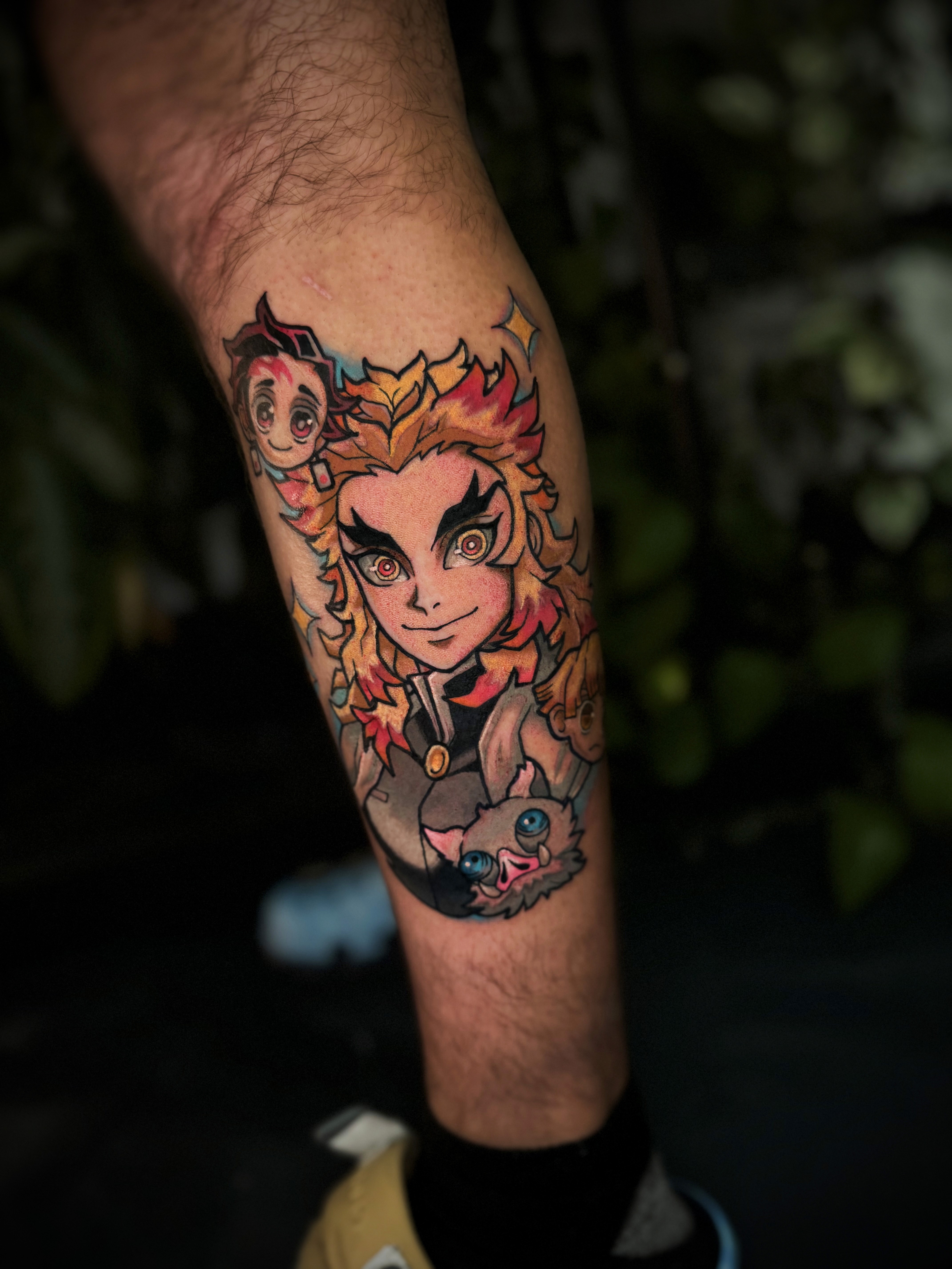 A vibrant tattoo of a chainsaw-like creature on a person's forearm. The tattoo is detailed with shades of orange, black, teal, and red.