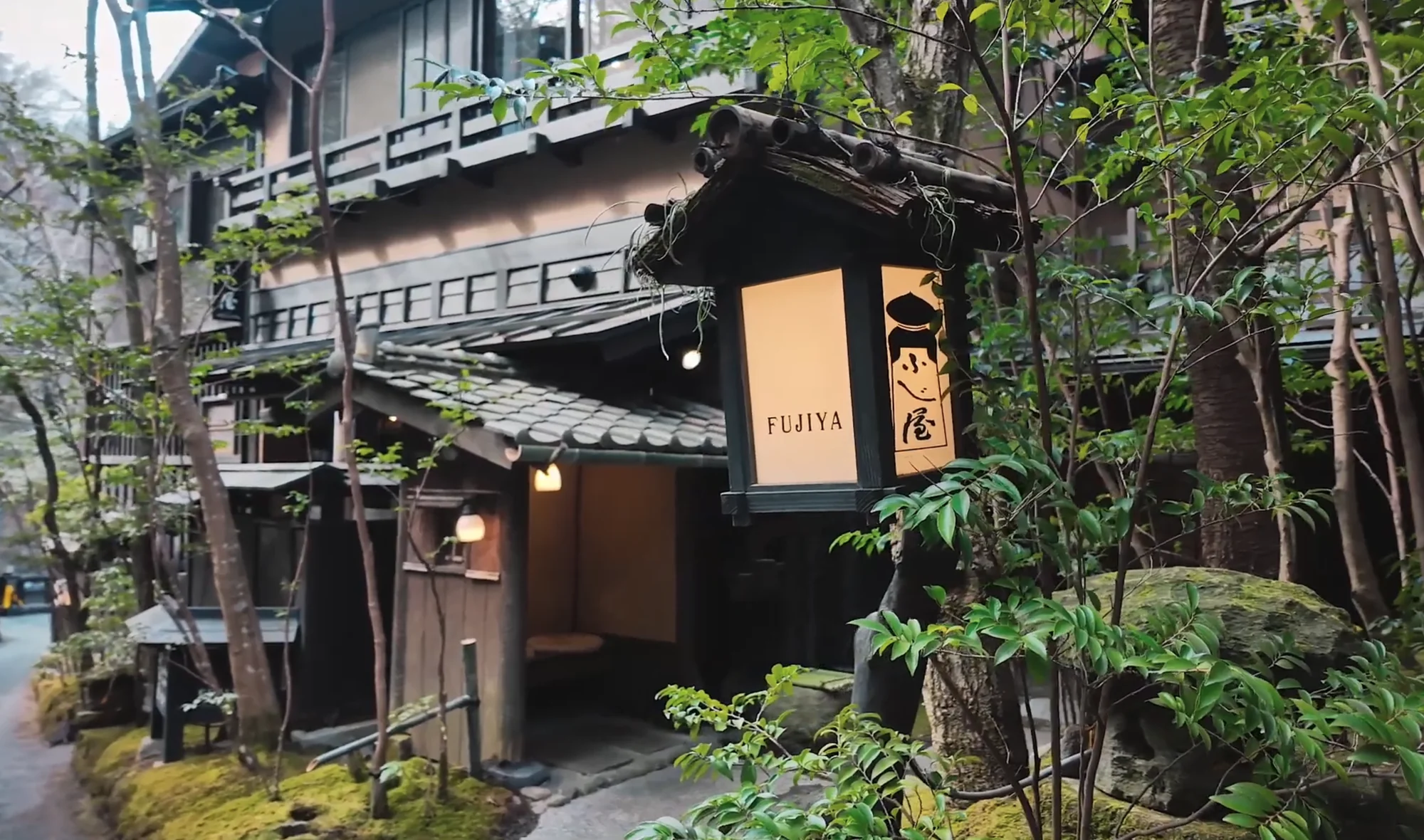 The timber frontage of Ryokan Fujiya with a lit entrance lantern and moss garden