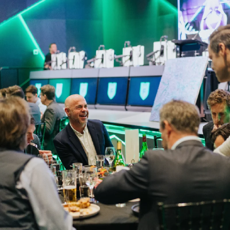 A group of men in suits are sitting down and having fun at a corporate event in the Alienware Arena