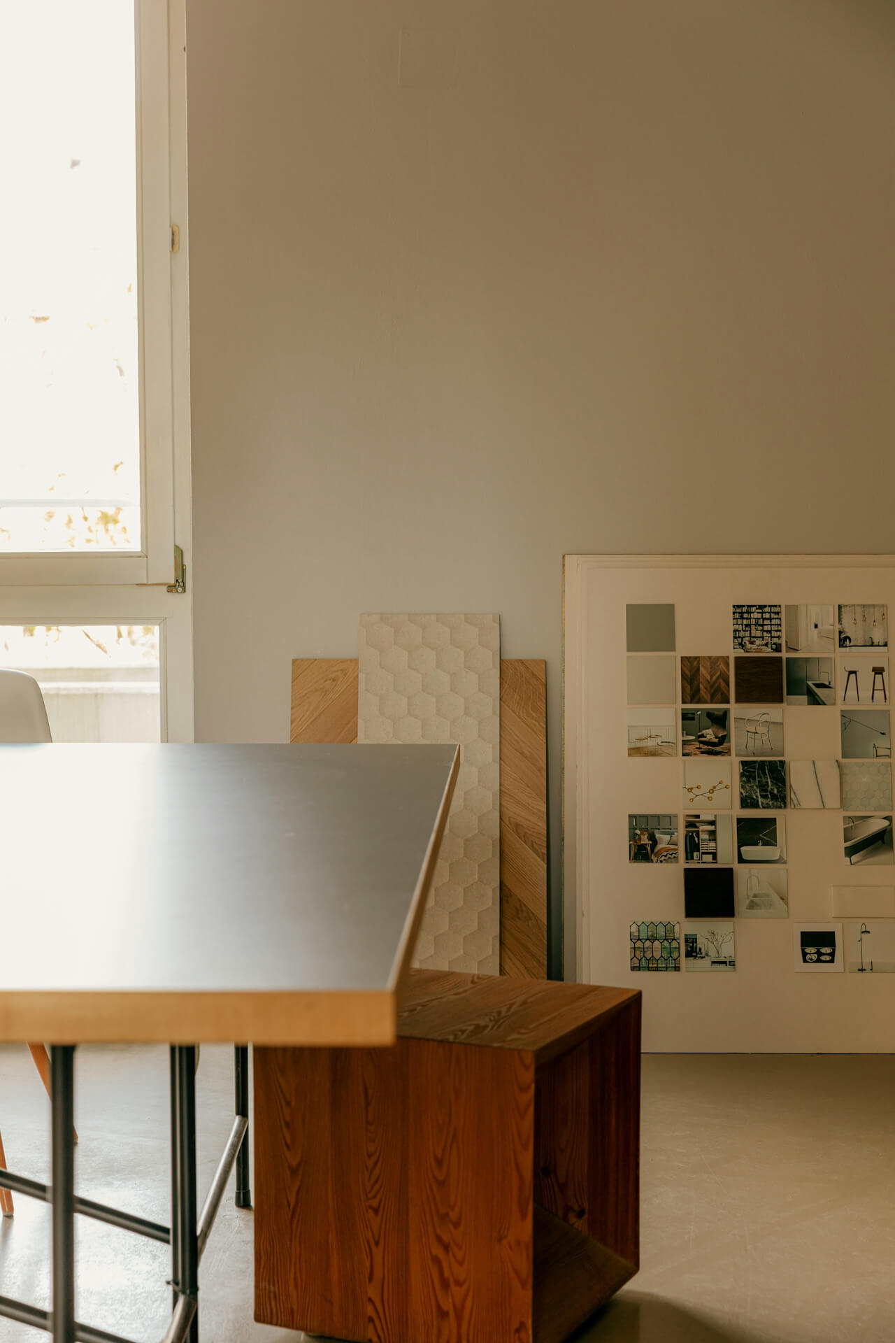 A minimalist room with a sleek table, wooden stools, and a collage of material samples on the wall. Soft lighting creates a calm, creative atmosphere.