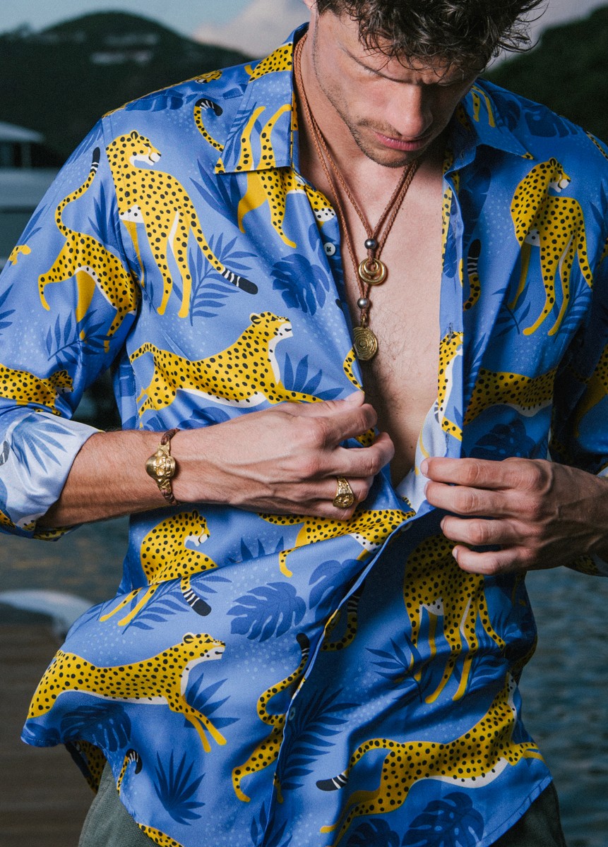 Fashion-forward man wearing bold gold medallions and Tahitian pearls over a colorful cheetah-print shirt, embracing tropical luxury style.