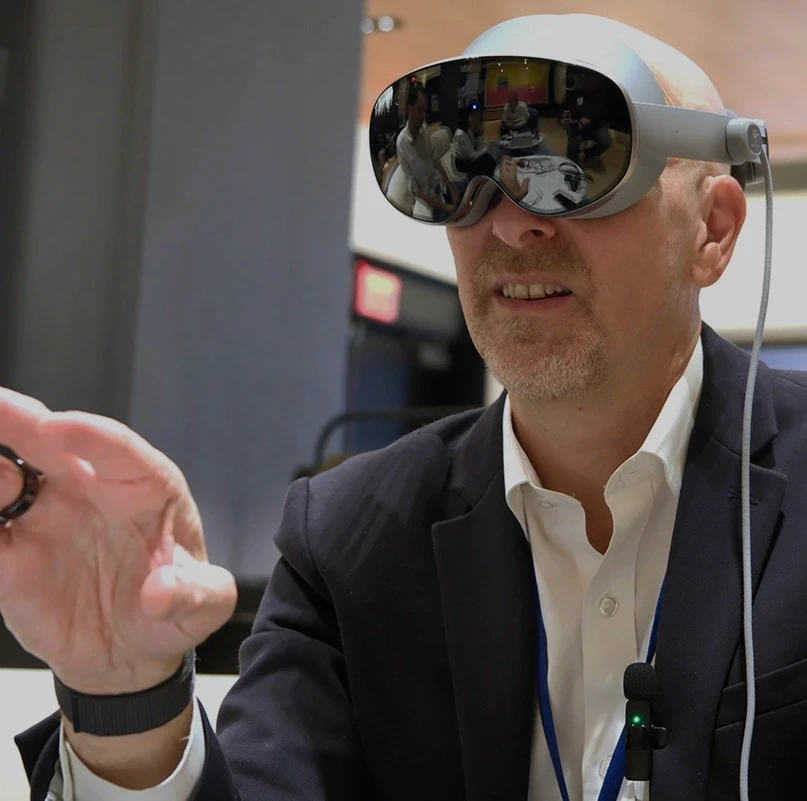Business professional wearing a Samsung Galaxy XR headset and gesturing with one hand at a corporate event
