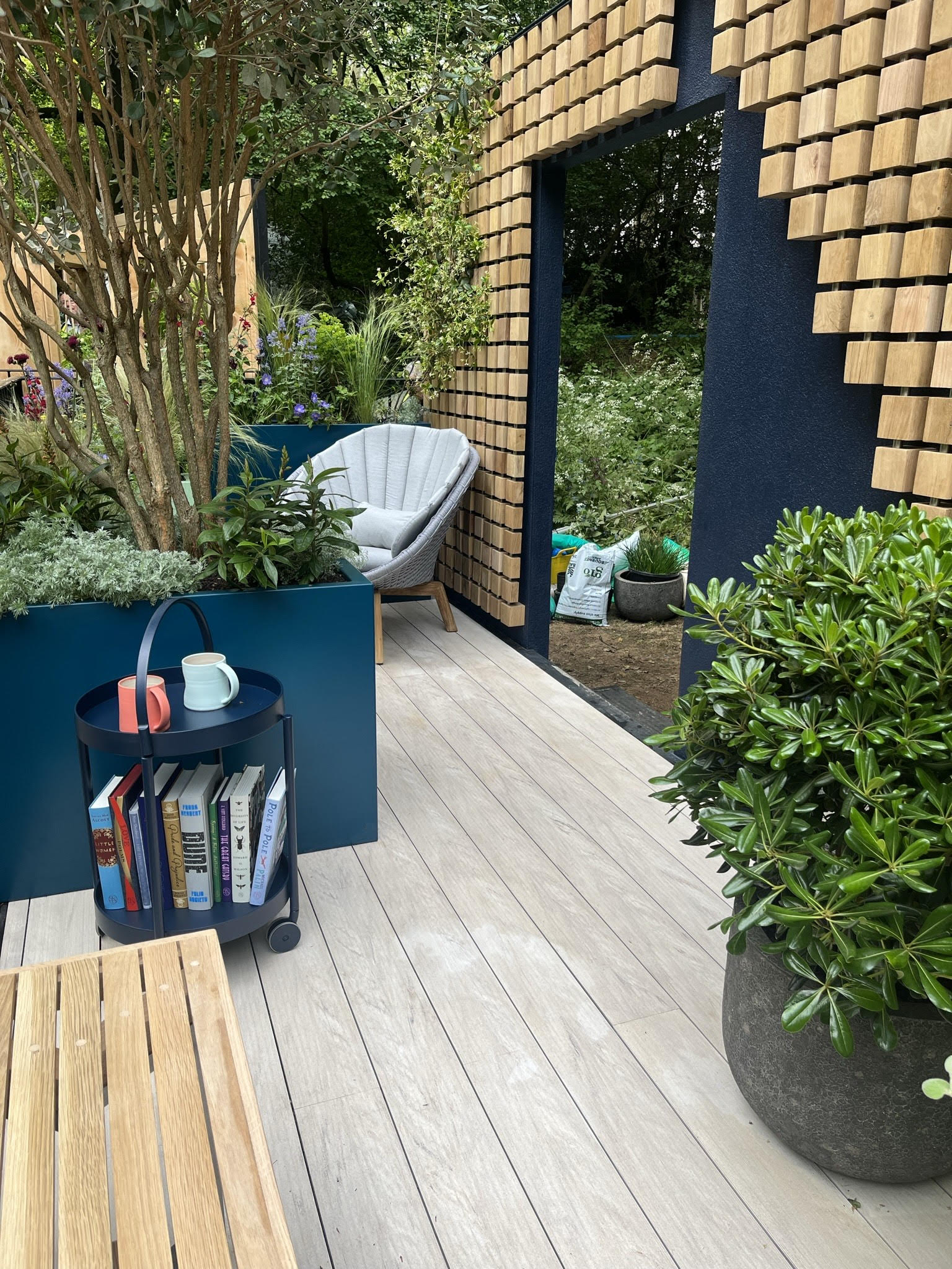 A wooden walkway leads to an open space with plants, modern decor, and a glimpse of an outdoor area.