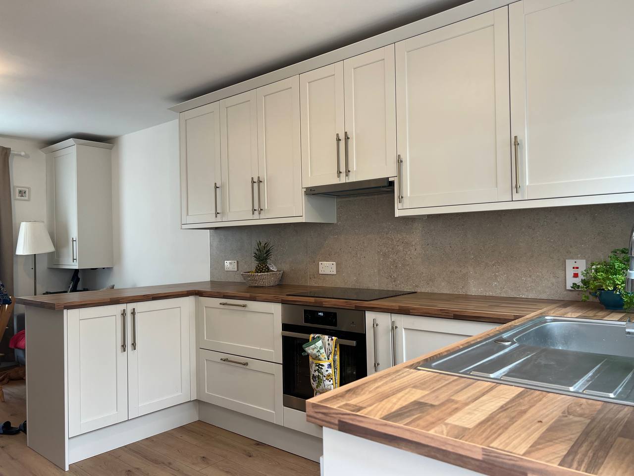 Modern living room with abstract art, beige sectional sofa, indoor plants, and large windows.
