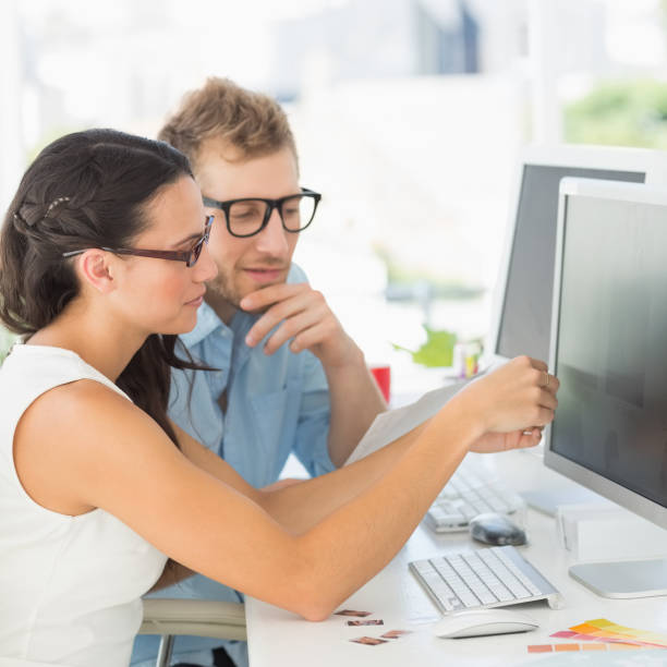 A man and woman sit together in front of a computer while one goes over the content of a document on-screen with the other