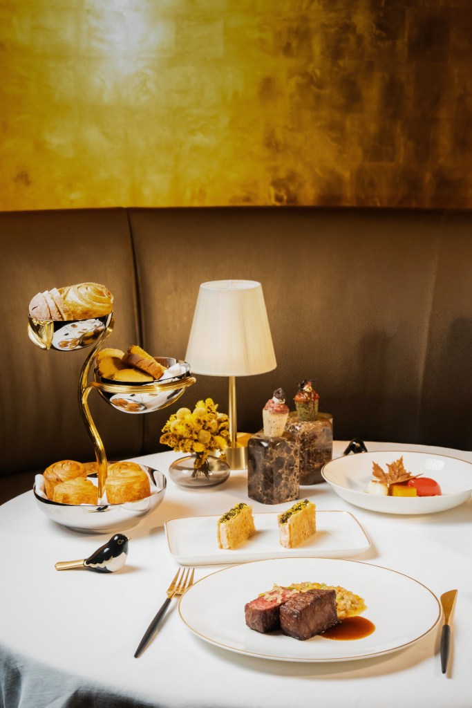 A beautifully arranged dining table featuring gourmet dishes, including a prominent plate of steak with sauce, side dishes, and an elegant display of pastries in a multi-tiered stand.