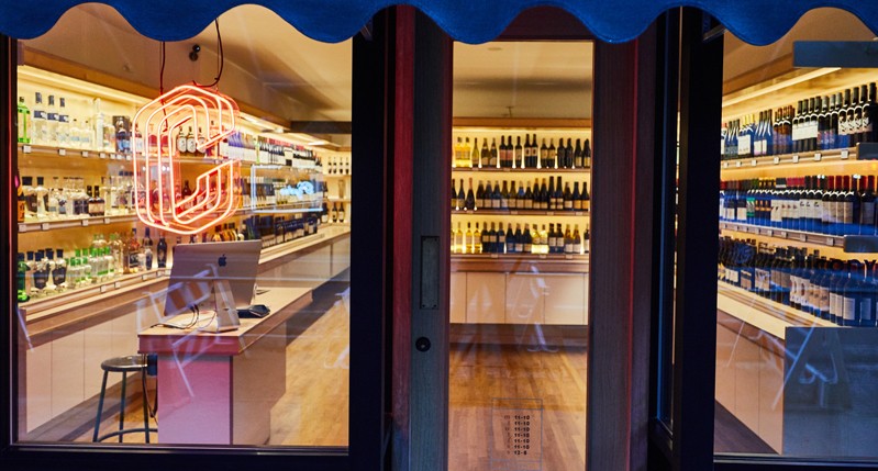 A photo of a store that sells different drinks. On the window there is a neon letter C.