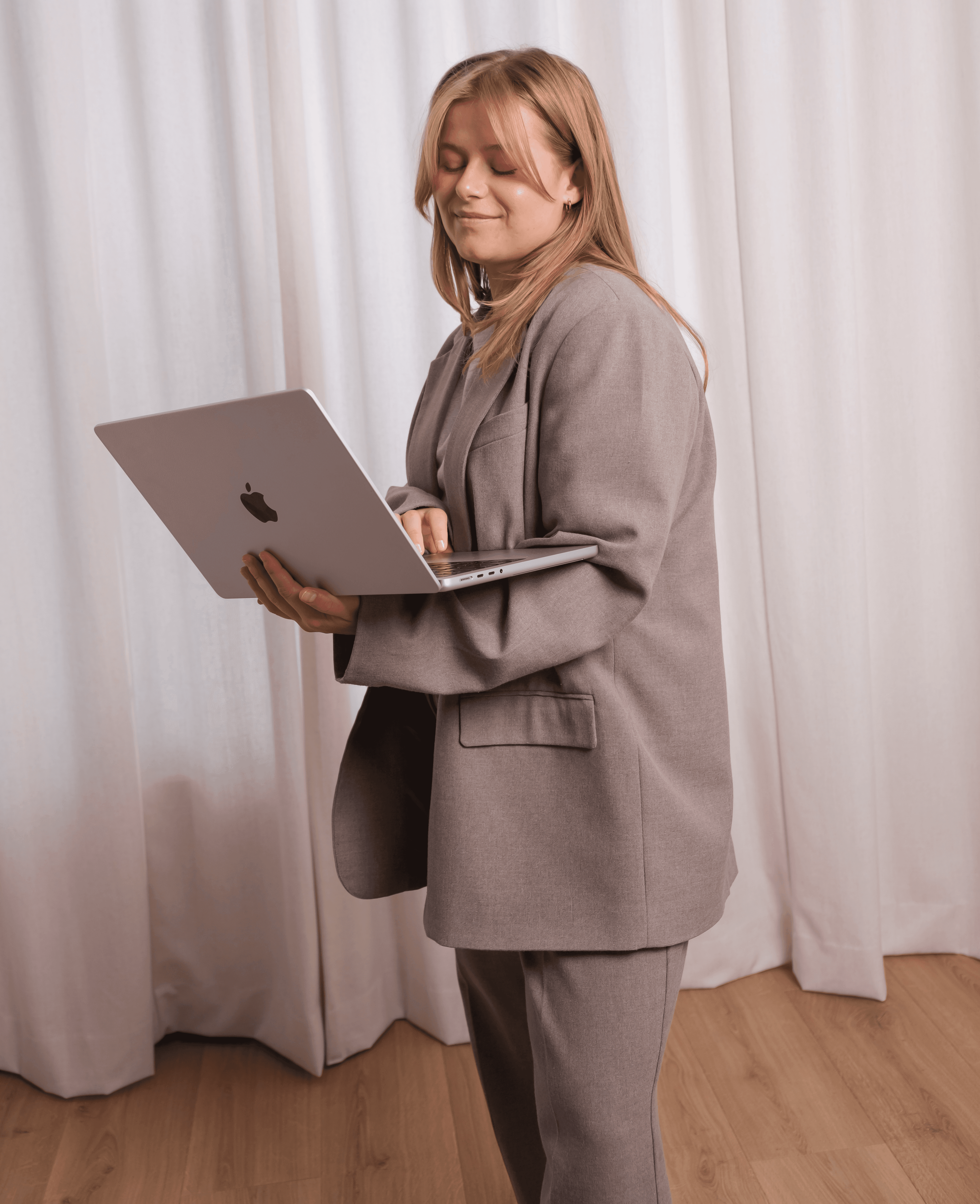A woman in a teal dress sits in a dimly lit room, focused on her smartphone. A laptop and notepad are on the glass table, suggesting a working environment.