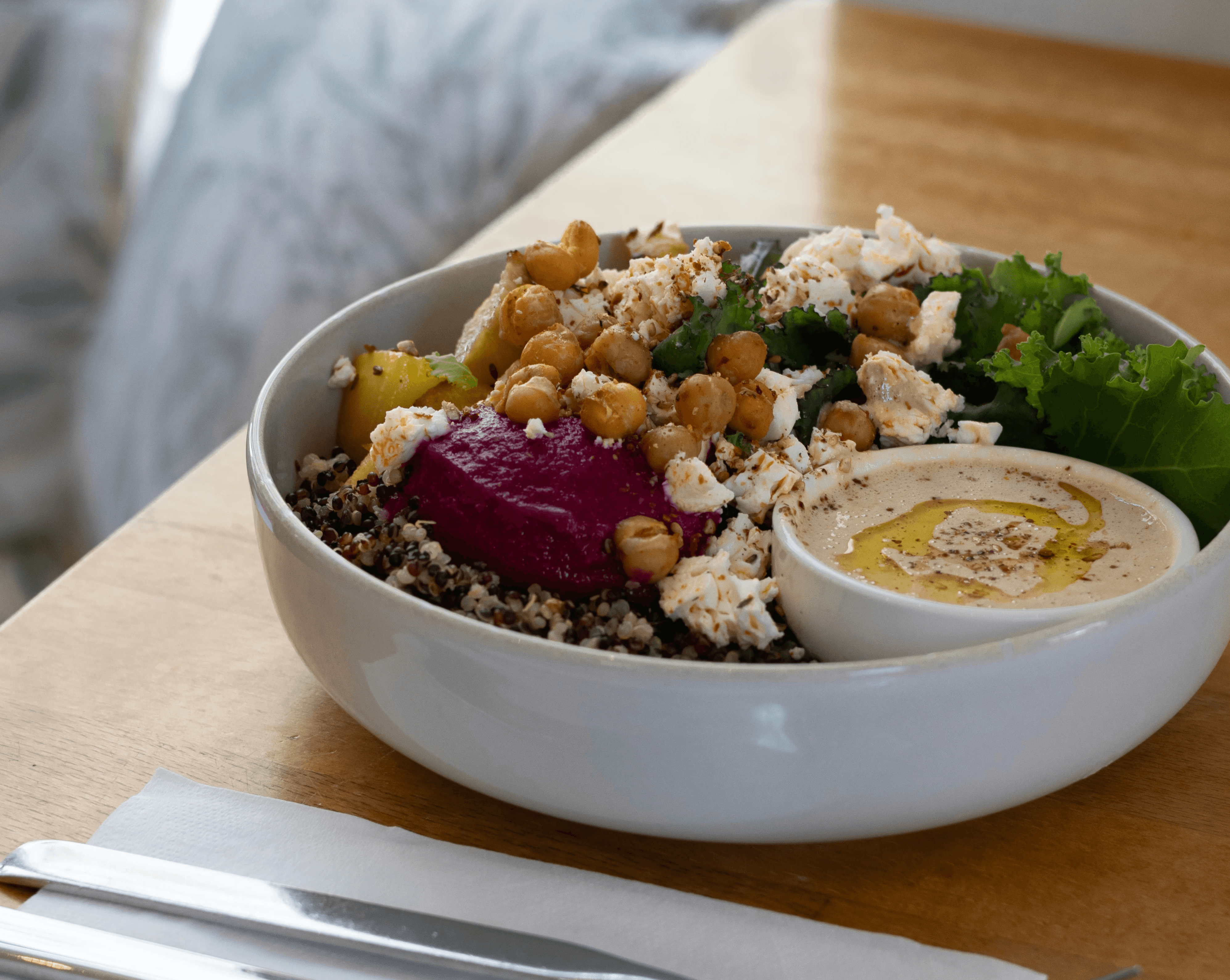 Bowl auf einem Tisch serviert gefüllt mit Salat, Quinoa, Kichererbsen, Feta, Hummus sowie Dip