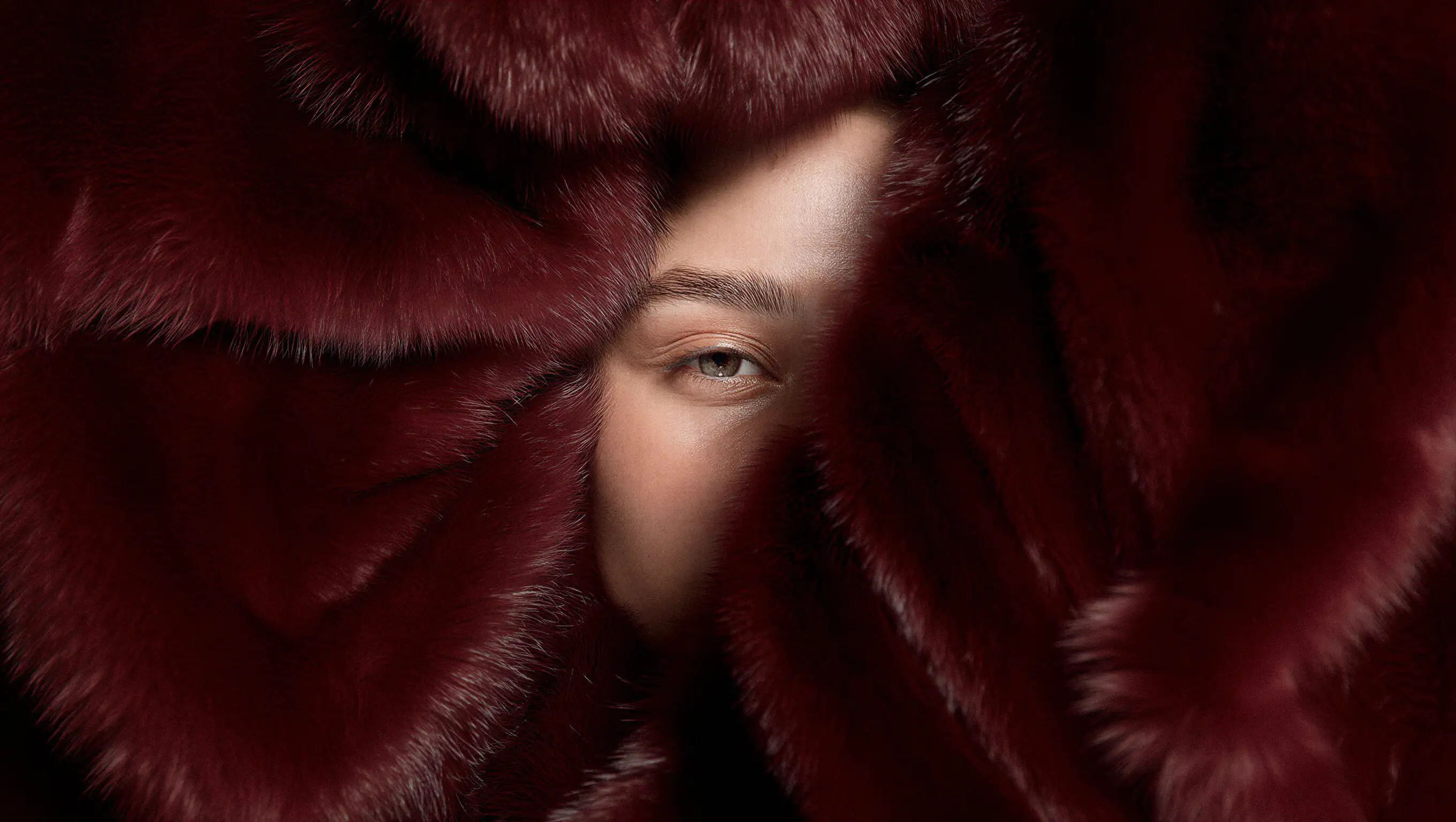 Atmospheric hero image for Laluvia featuring a close-up of a person's eye partially obscured by rich burgundy fur textures with the minimalist white brand logo.