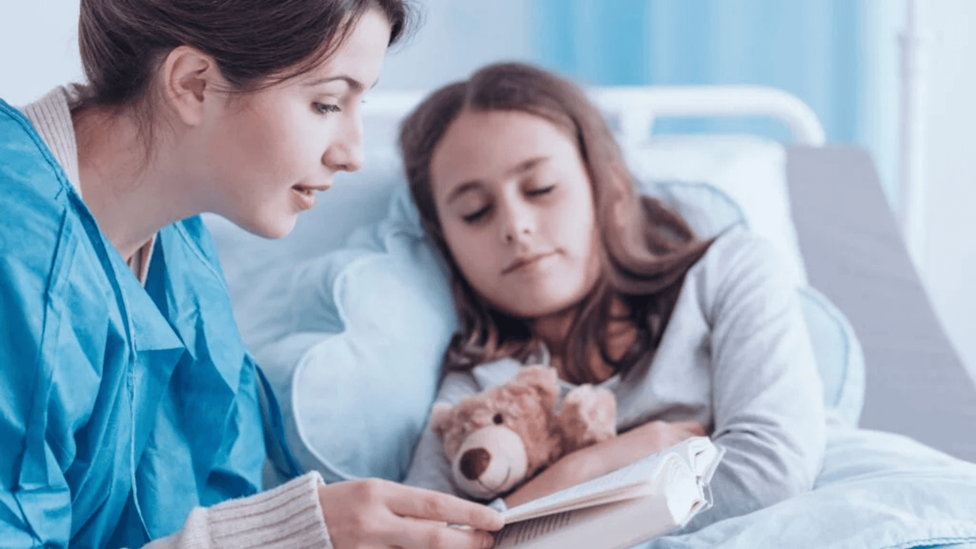 Healthcare professional reading a book to a young girl resting in a hospital bed, with the child holding a teddy bear