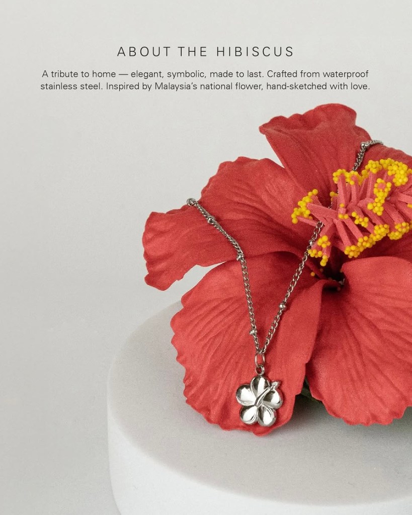 A silver Hibiscus pendant necklace resting on a vibrant red Hibiscus flower, symbolizing Malaysia's national flower and celebrating home and memories.