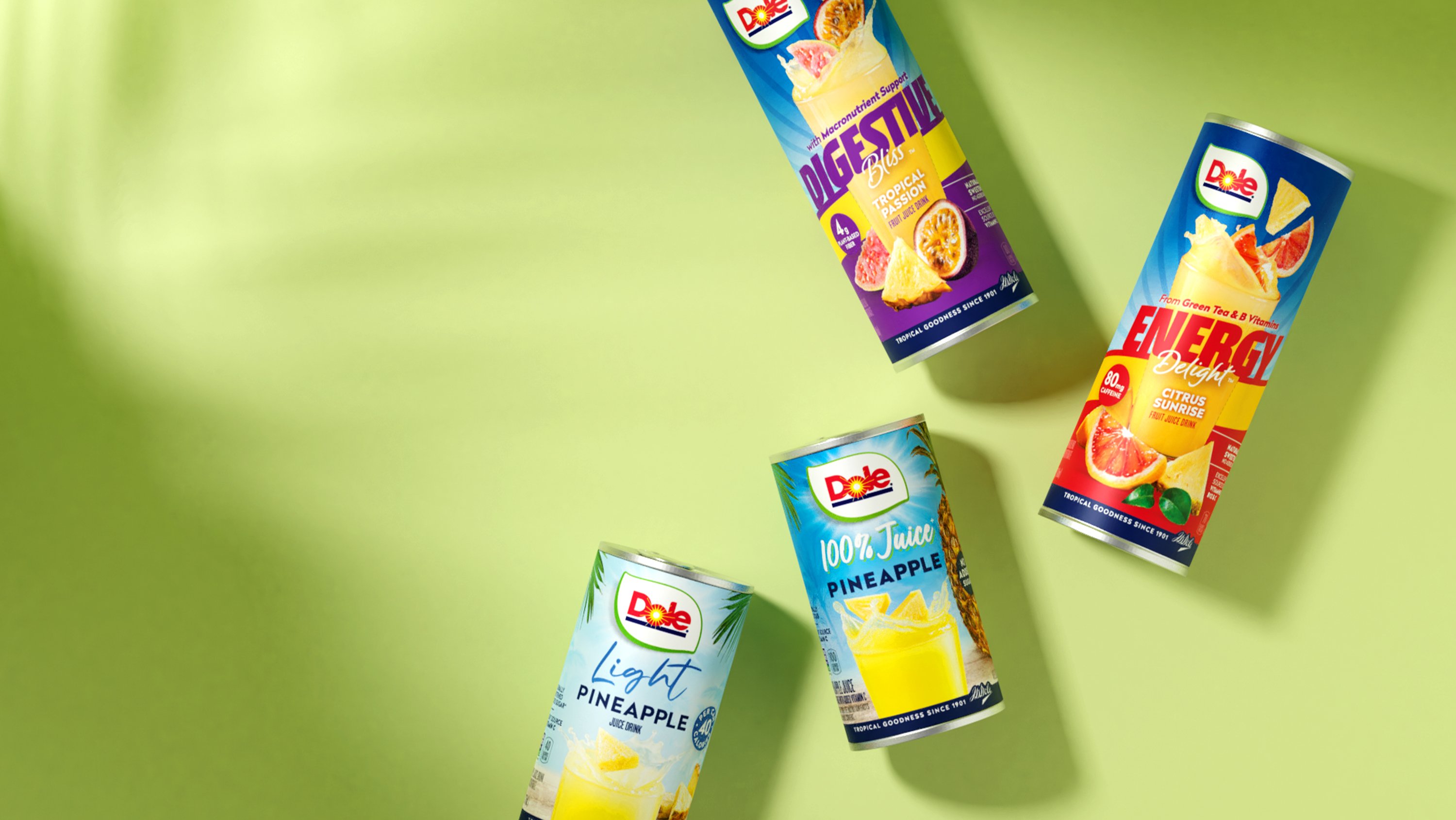 Four colorful tropical fruit juice cans from Dole are arranged on a light green background, casting soft shadows. The labels are vibrant and eye-catching.