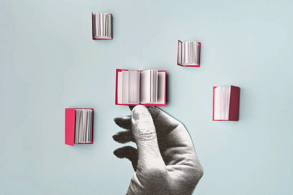 Collage-style image of a hand holding an open book while several small books float around on a light background.