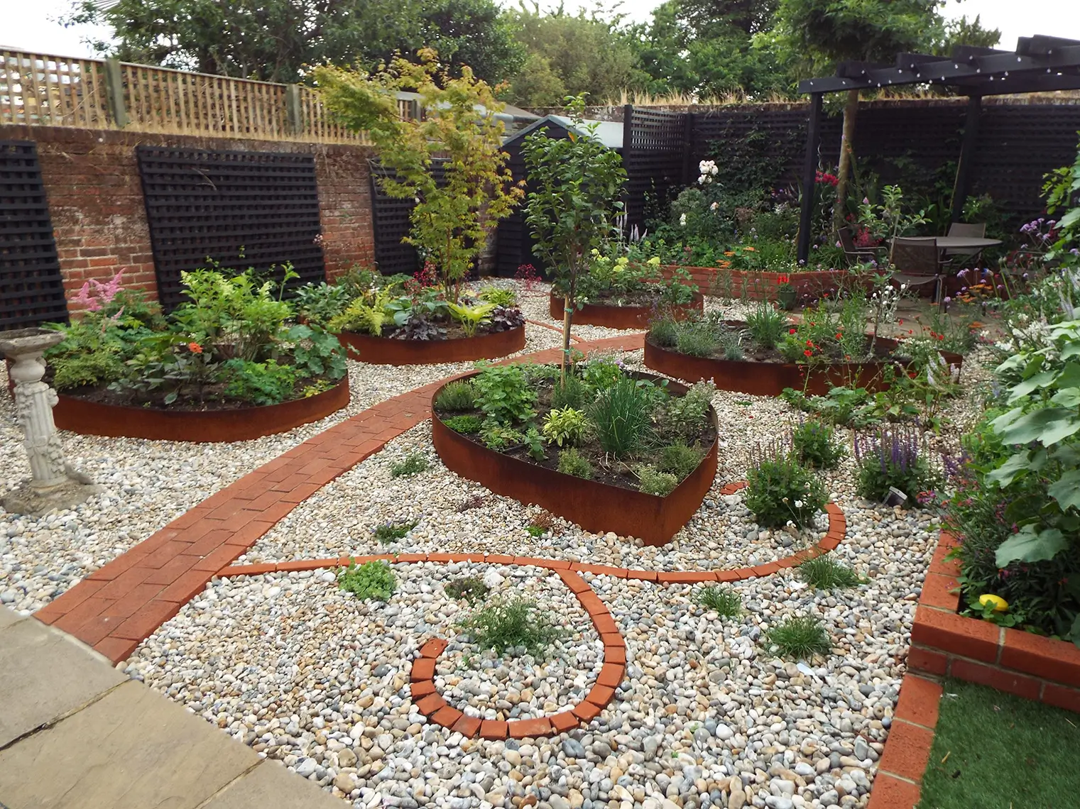 A lush garden featuring circular flower beds, pathways, and a variety of green plants and shrubs.