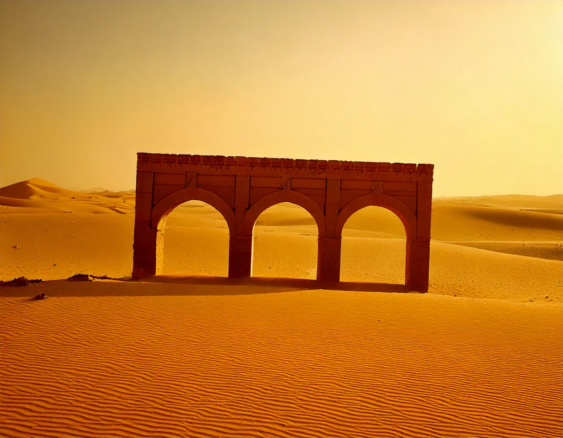 Un paysage désertique avec des dunes ondulées et une architecture ruinée. L'arc en plein cintre fait écho à l'héritage de l'architecture byzantine et islamique, évoquant une atmosphère de mystère et de grandeur ancienne dans un environnement aride.