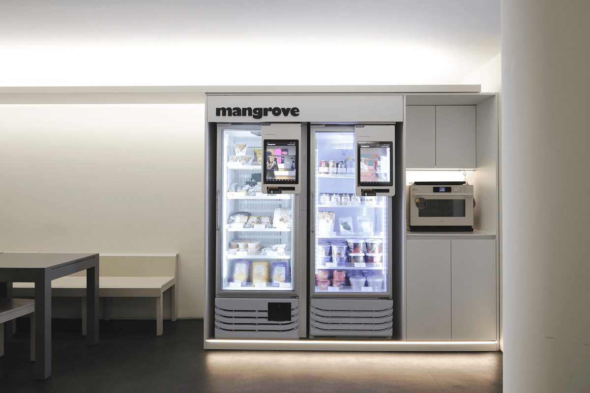 Mangrove food vending machine with an oven and microwave on the right and a small dining area with tables and chairs on the left.