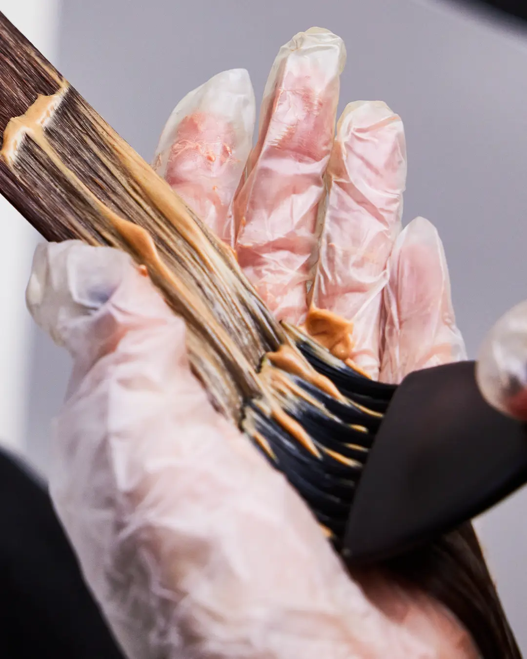 A person holding a section of hair, applying hair colour with a brush.