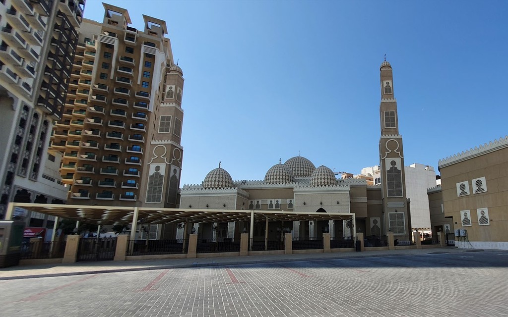 Mosque in Al Jaddaf with domes, twin minarets, and urban skyline backdrop on a clear sunny day.