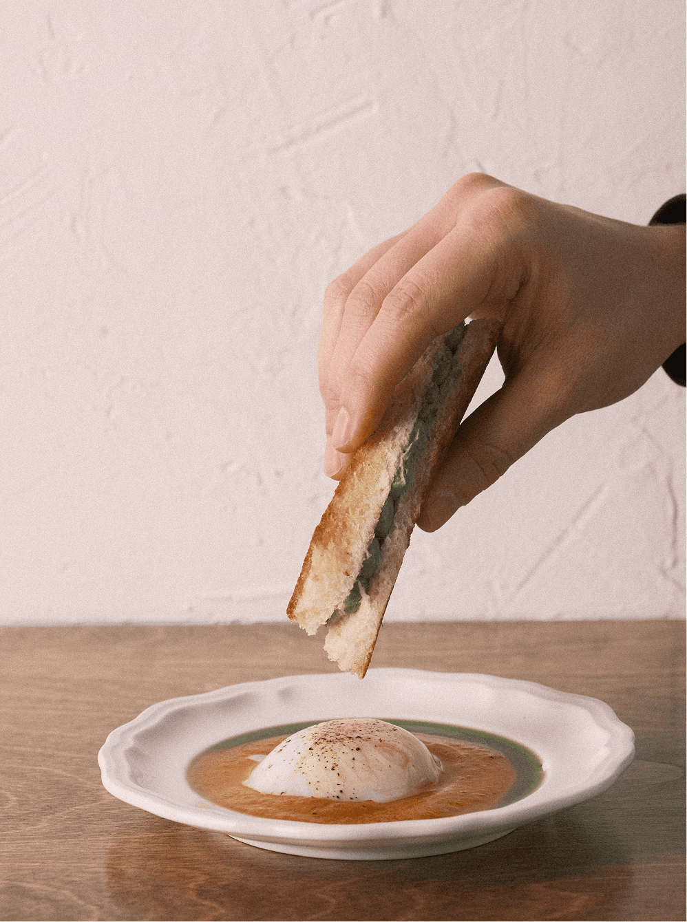 Une main trempe un pain brioché dans sa purée de courge et oeuf mollet.