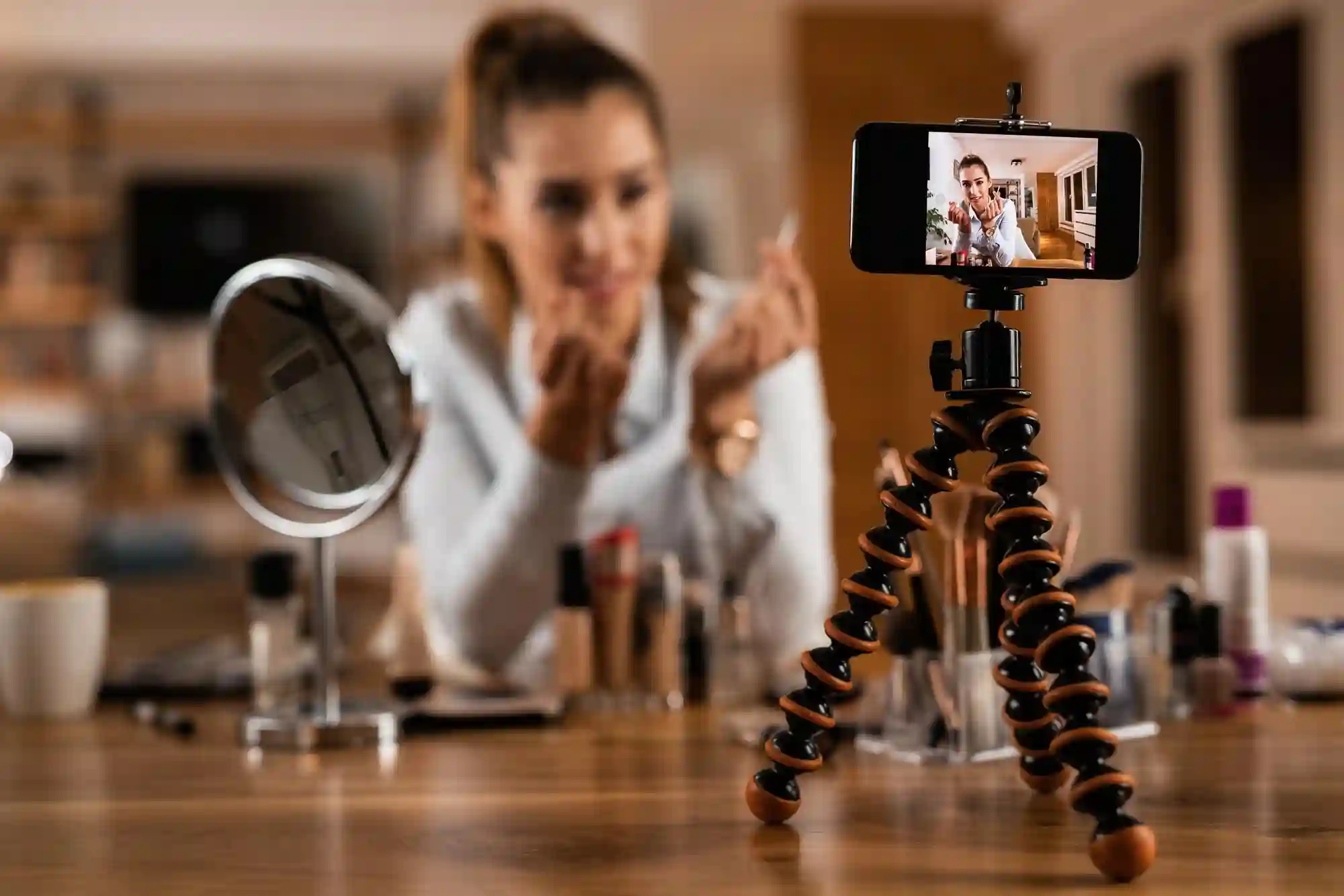 A female beauty influencer filming a makeup tutorial on her smartphone using a tripod for a social media blog.