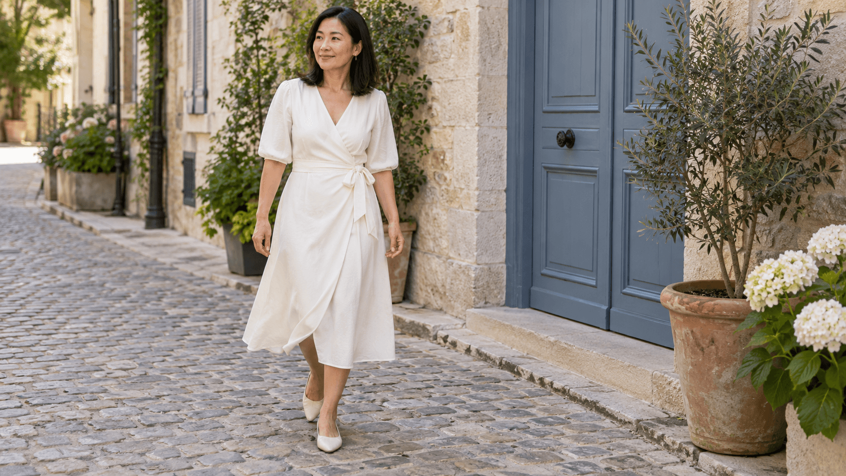 Robe portefeuille ivoire midi à lien sur le côté, portée dans une ruelle pavée.
