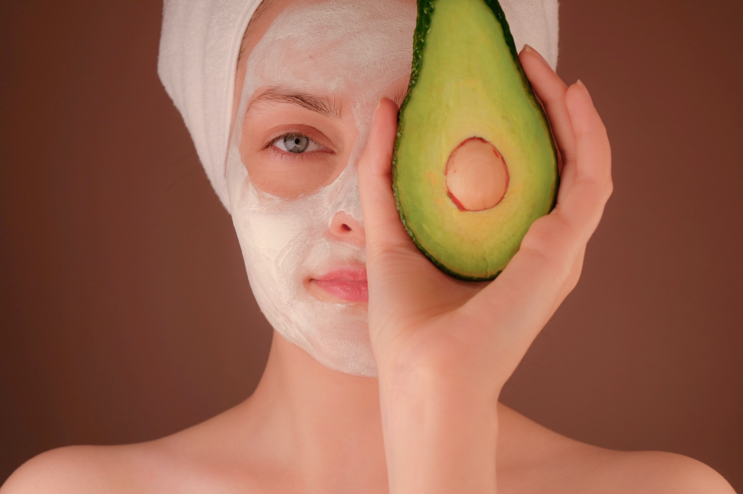 woman with a facemask holding half an avocado in front of her face