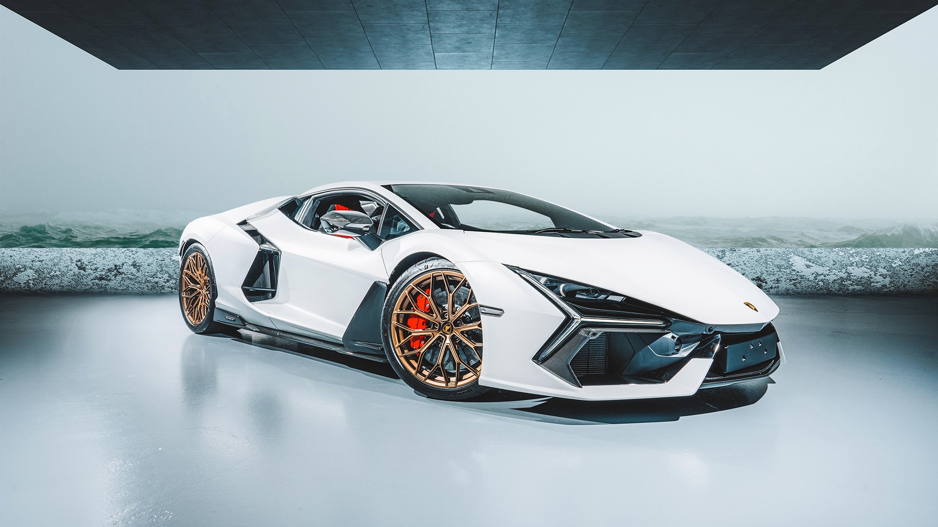 White Lamborghini Revuelto with bronze wheels in front three-quarter view, studio-lit against a cool grey backdrop, its angular carbon front splitter, Y-shaped headlights and red calipers in frame, reflected on the glossy floor.