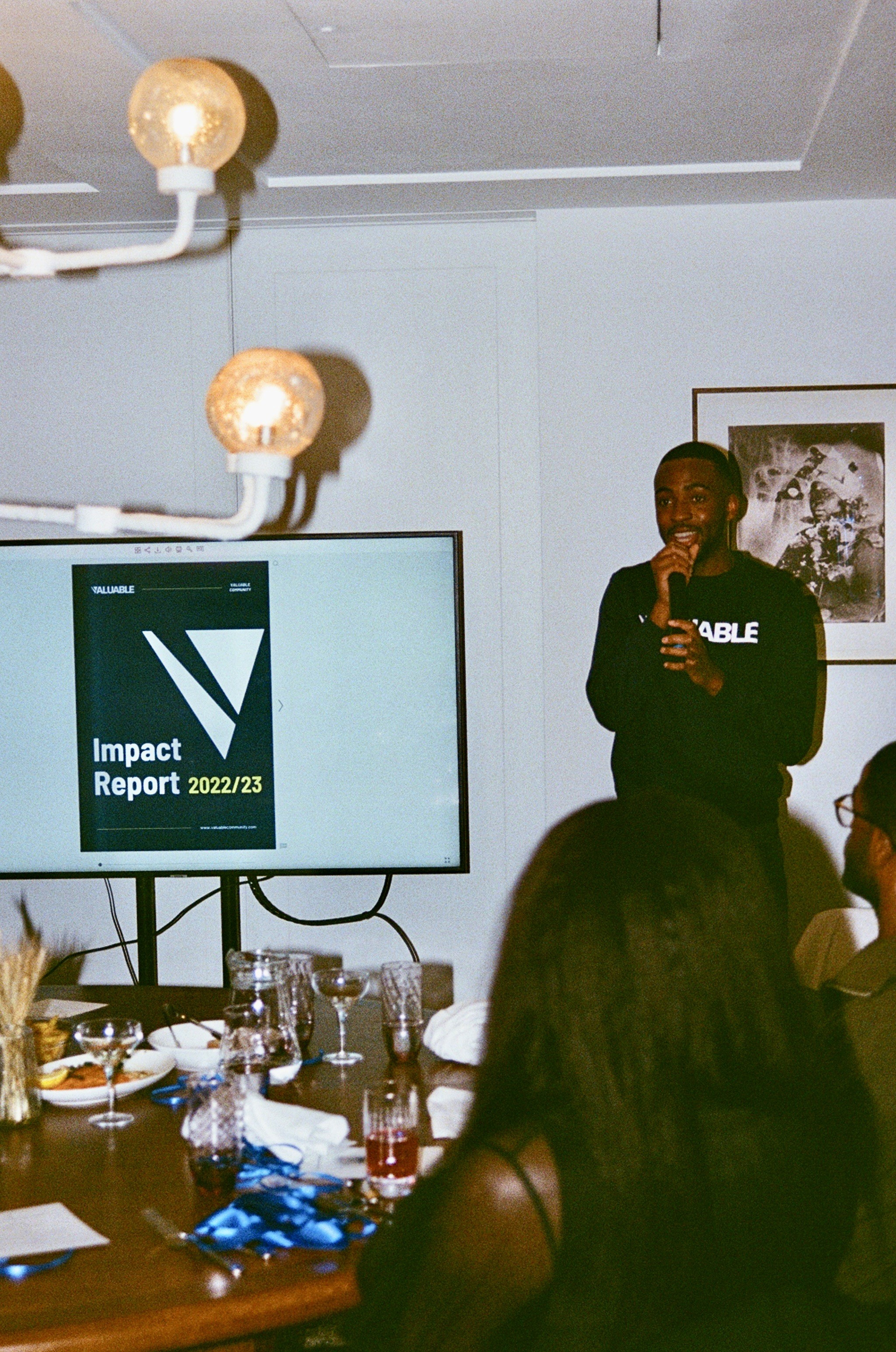 Man presents Valuable Impact Report 2022/23 on screen at a meeting with attendees.