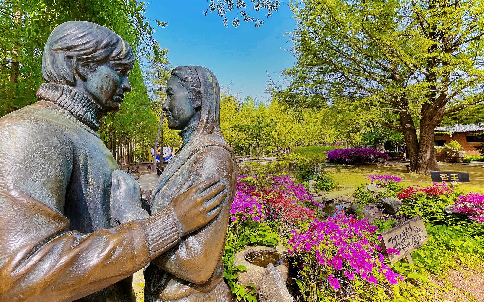 تمثال لزوجين محاط بالزهور الملونة والأشجار في جزيرة نامي، كوريا الجنوبية.